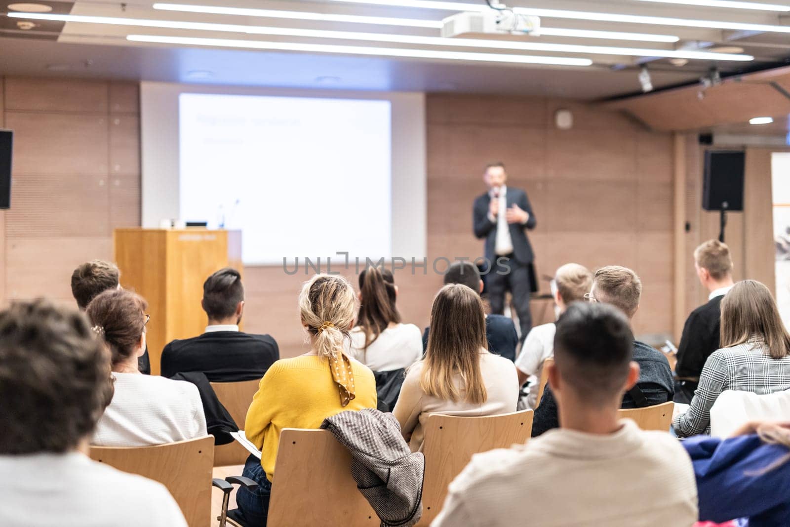 Speaker giving a talk in conference hall at business event. Rear view of unrecognizable people in audience at the conference hall. Business and entrepreneurship concept