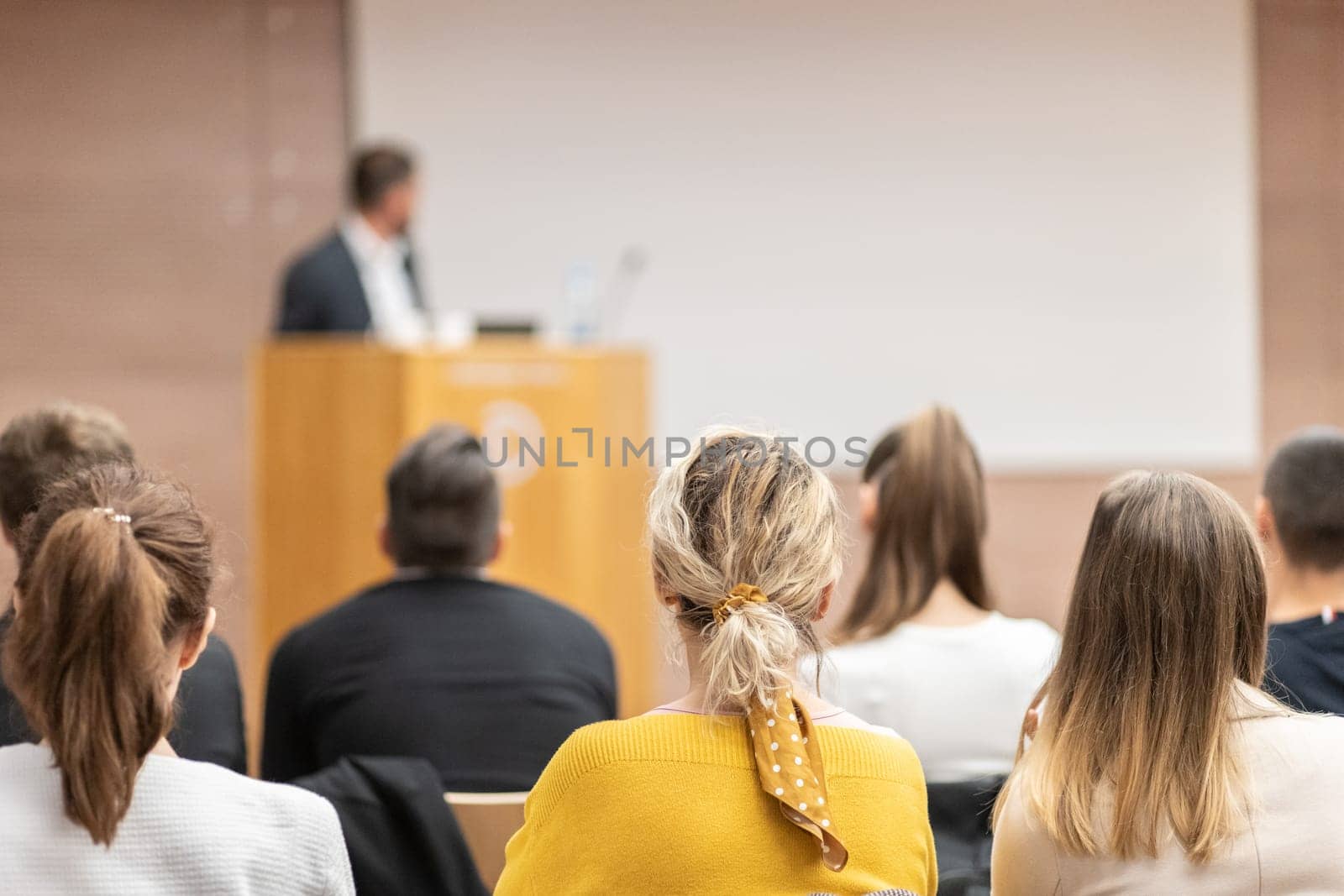 Speaker giving a talk in conference hall at business event. Rear view of unrecognizable people in audience at the conference hall. Business and entrepreneurship concept