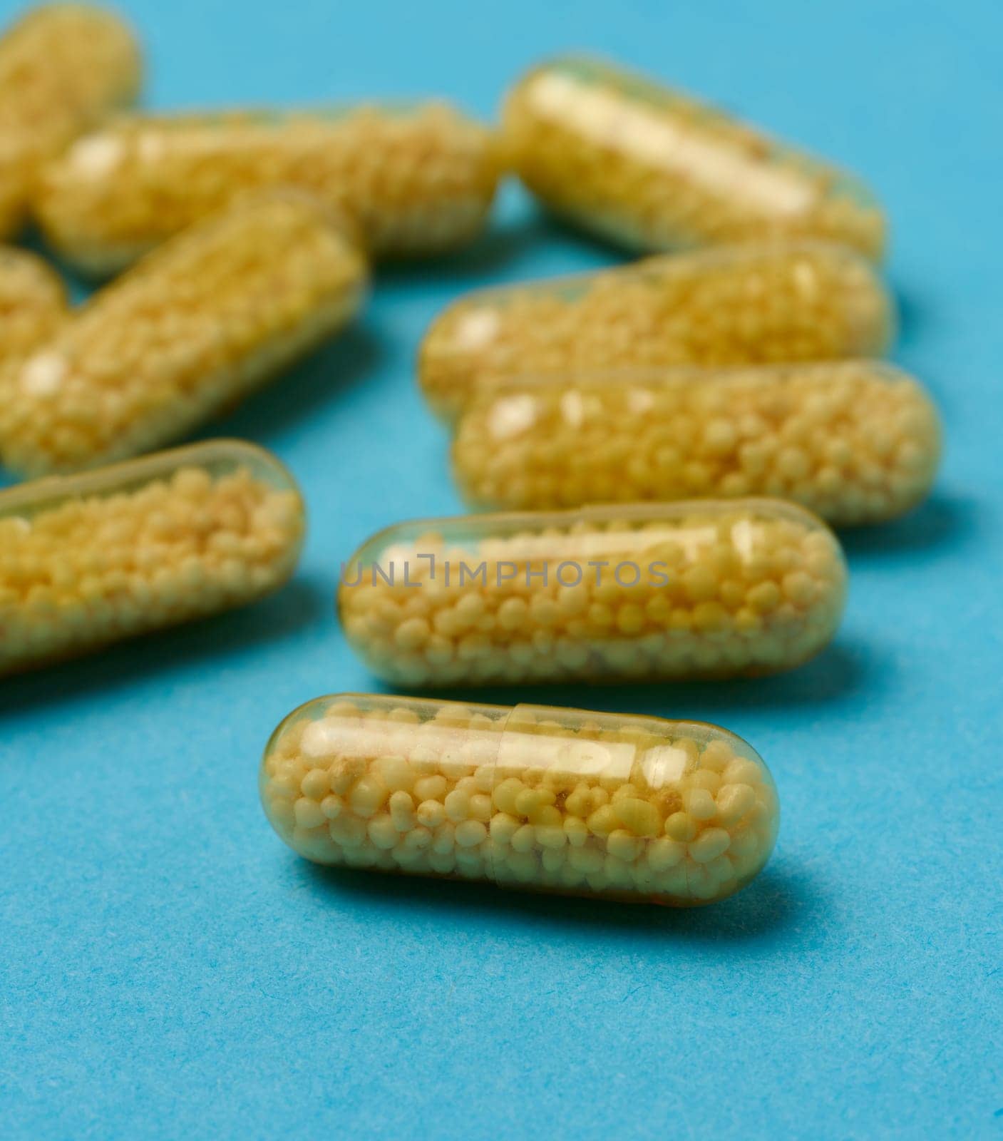 Transparent medical capsules with yellow granules inside on a blue background, tablets for treatment, vitamins
