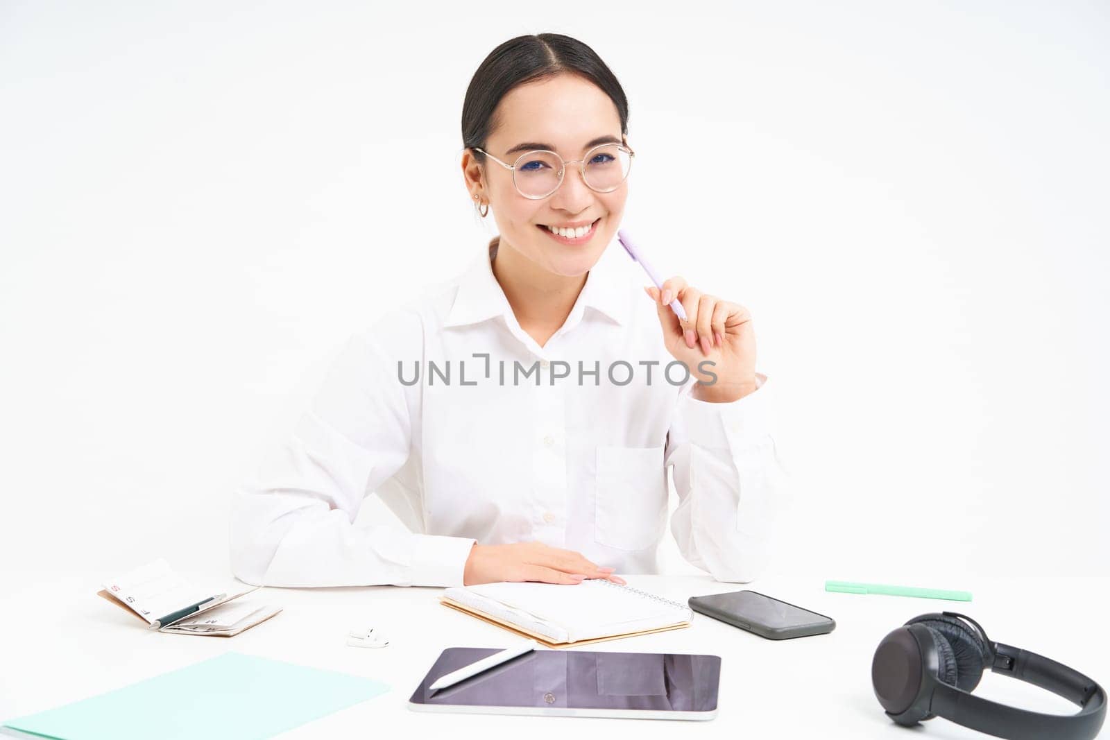 Office work and business. Young professional female employer, team leader sitting at workplace with digital tablet, smiling at camera, white background.