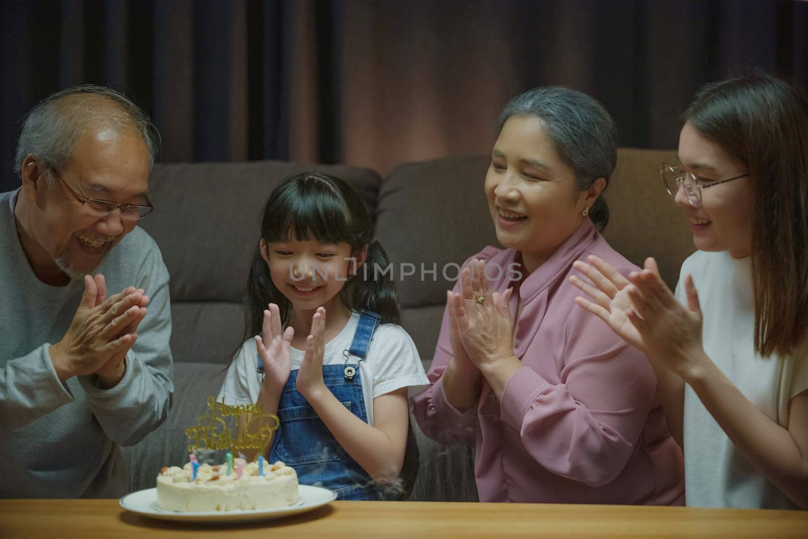 Birthday surprise. Happy Asian family grandparents and mother celebrating enjoy birthday party with cake of granddaughter at home in night time