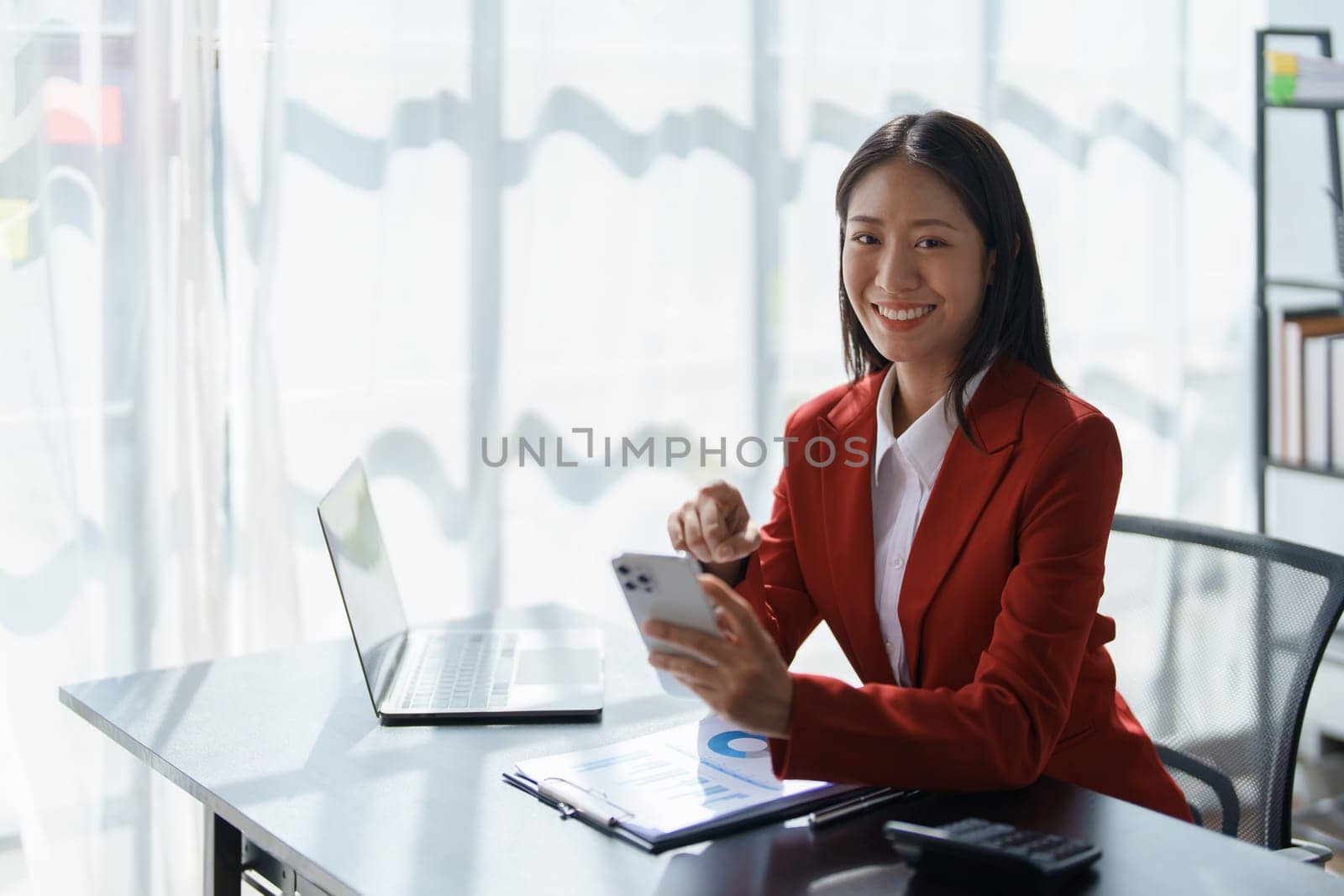 Portrait of beautiful young businesswoman standing smiling and using smartphone.