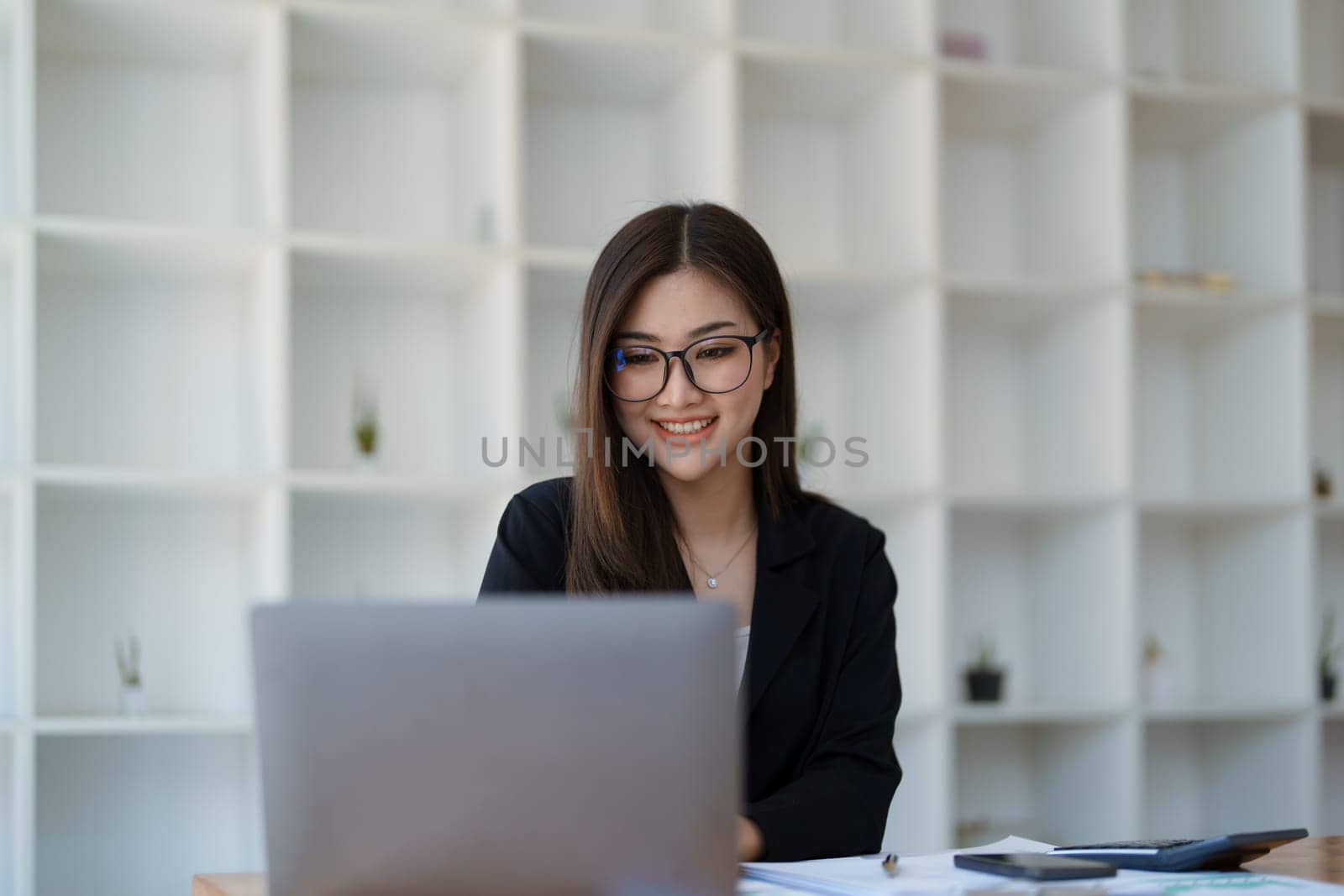 Portrait of a woman business owner showing a happy smiling face as he has successfully invested her business using computers and financial budget documents at work.