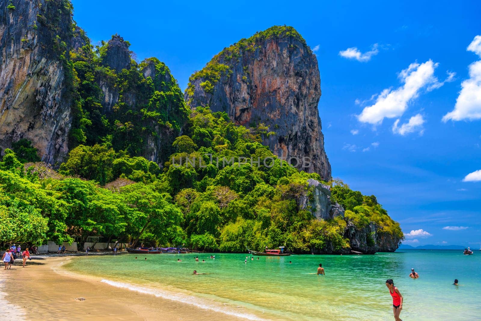 Rocks, water, tropical white sand beach and people swimming in emerald azure water of bay, Railay beach west, Ao Nang, Krabi, Thailand.