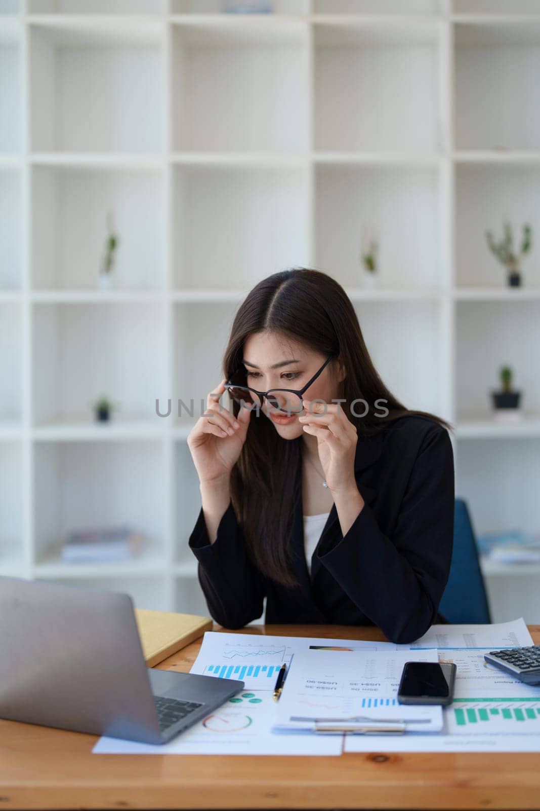 Young asian businesswoman manager, lawyer or company employee holding accounting bookkeeping documents checking financial data or marketing report working in office with laptop. Paperwork management.