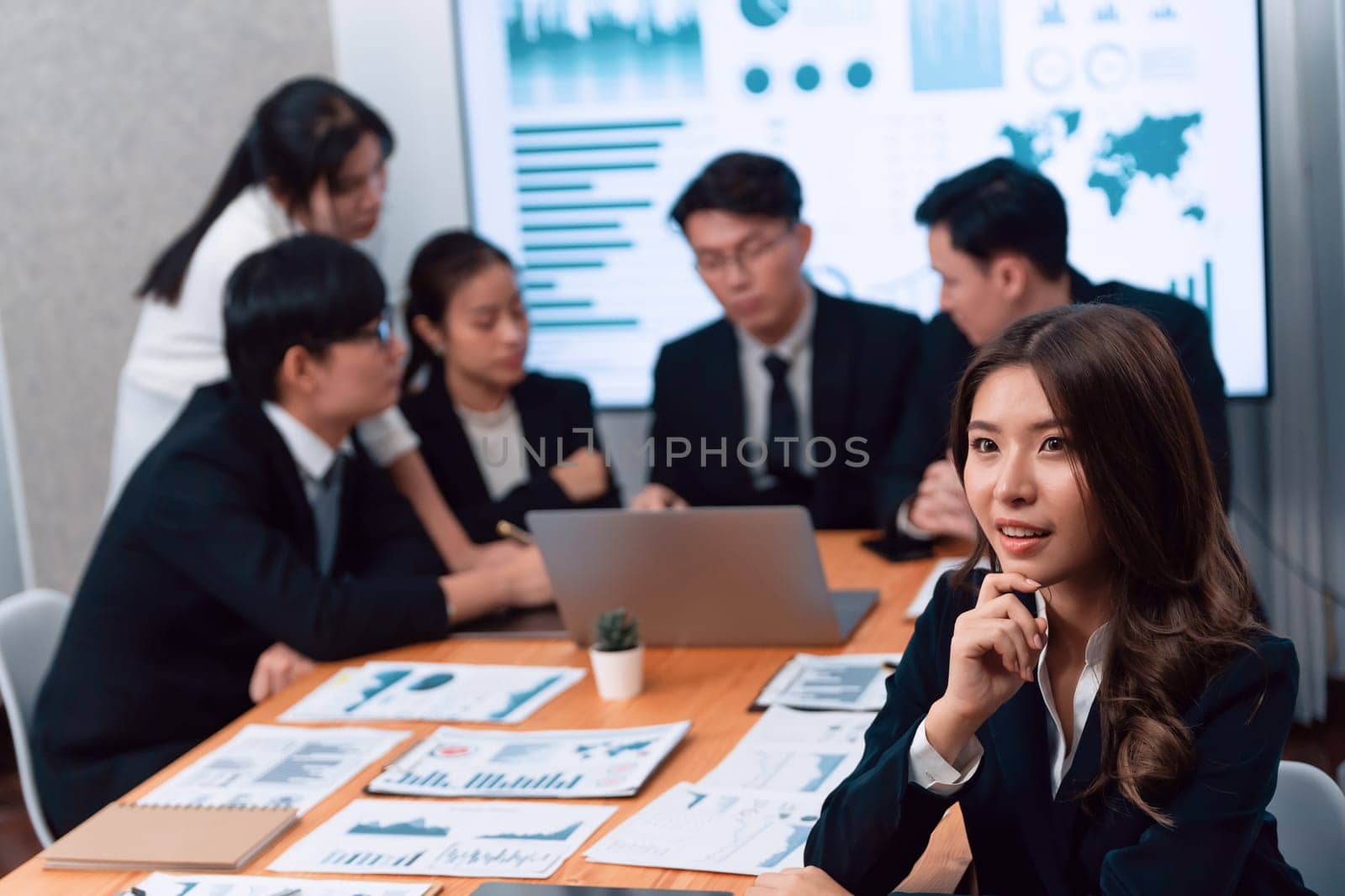 Focus portrait of female manger, businesswoman in the harmony meeting room with blurred of colleagues working together, analyzing financial paper report and dashboard data on screen in background.