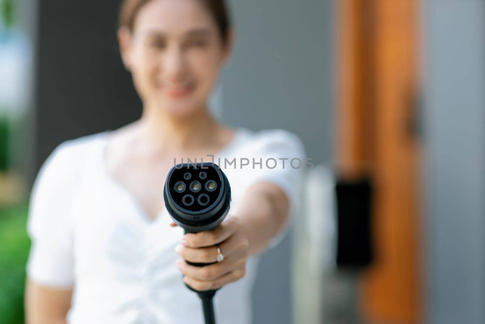 Focus hand pointing EV charger plug at camera with progressive blur background. by biancoblue