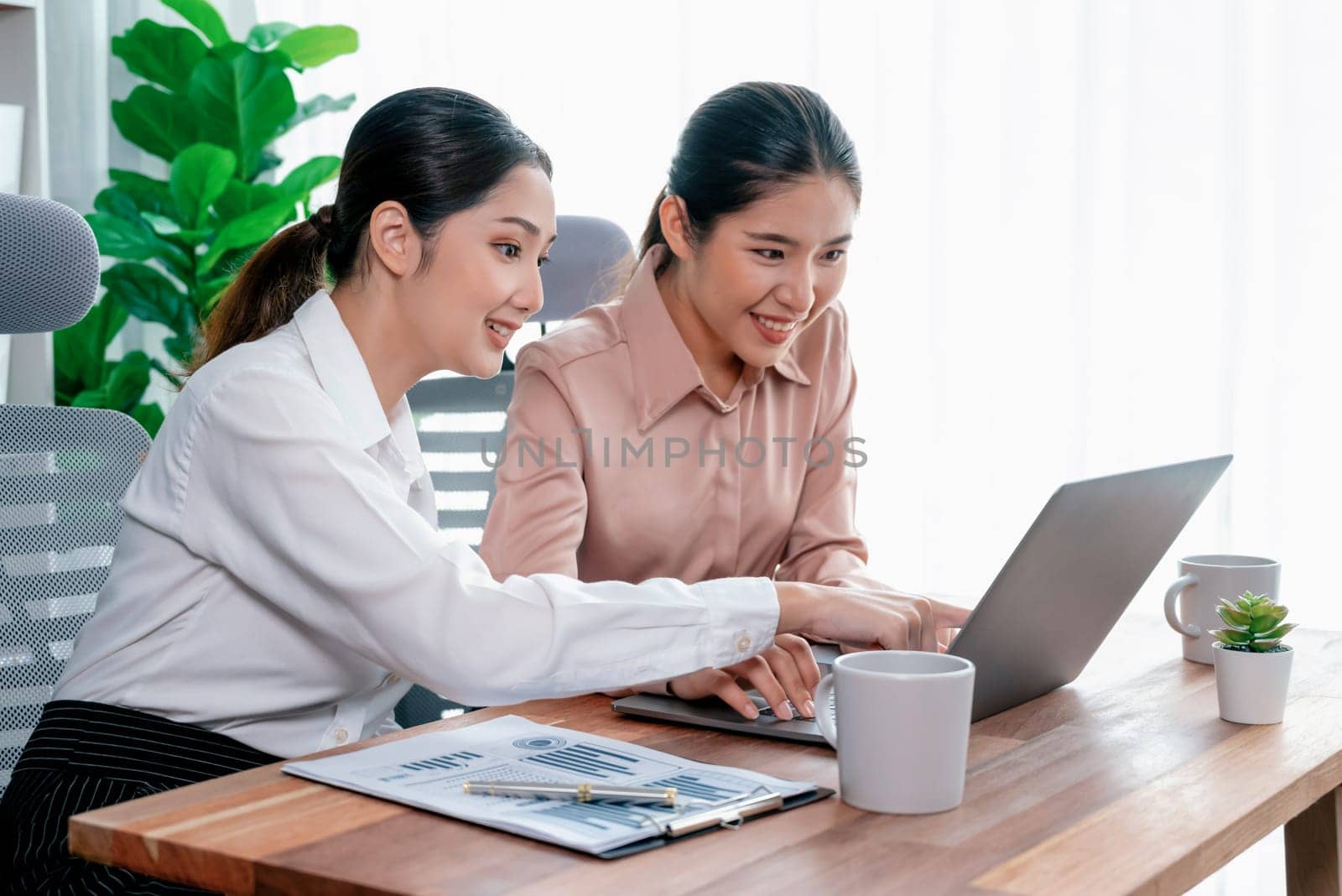 Two young businesswoman work together in office workspace. Enthusiastic by biancoblue