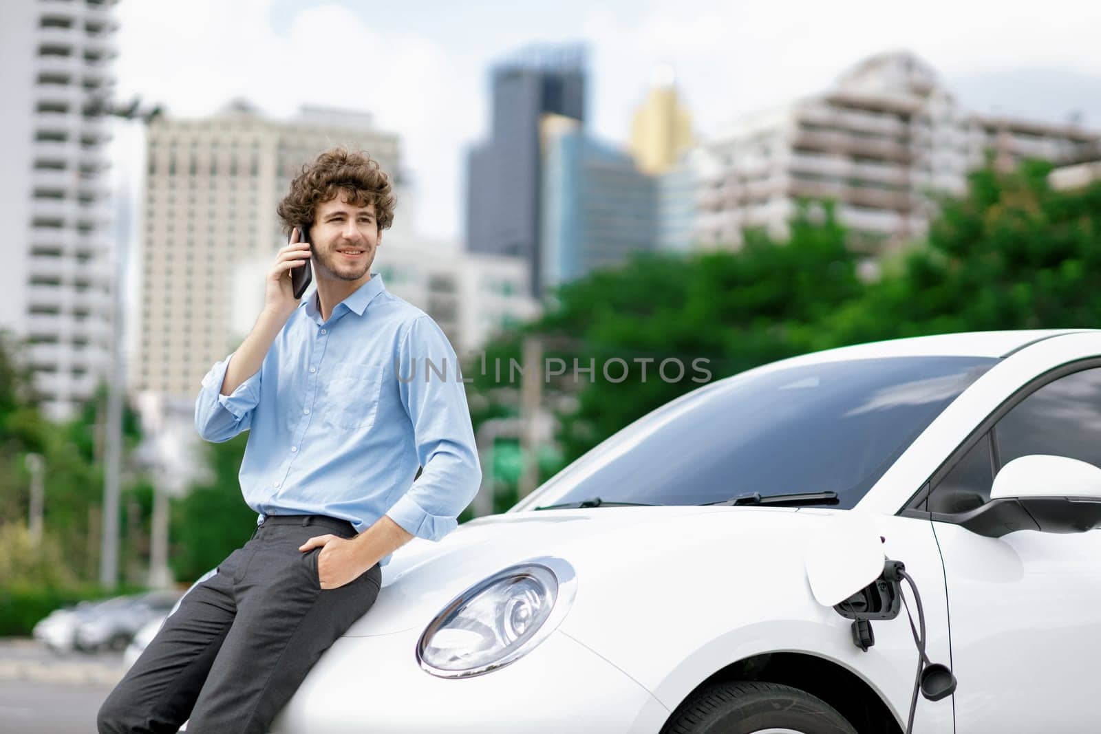 Progressive businessman talking on the phone with recharging electric vehicle. by biancoblue