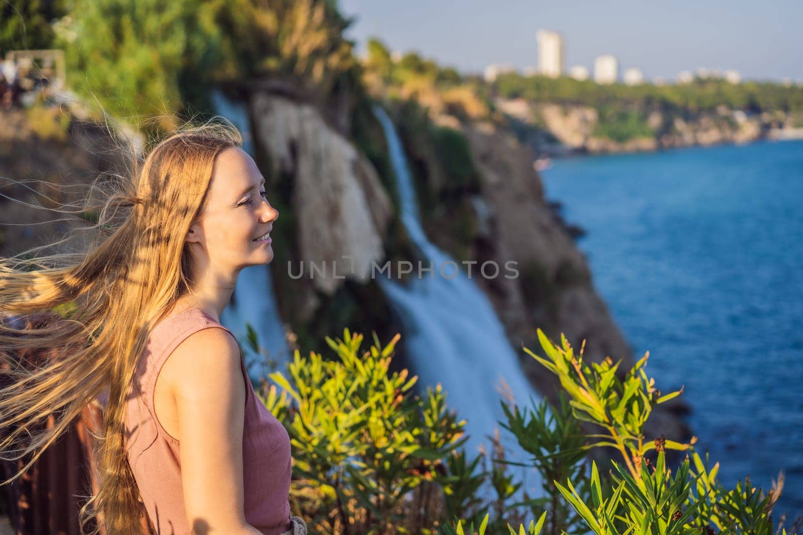 Beautiful woman with long hair on the background of Duden waterfall in Antalya. Famous places of Turkey. Lower Duden Falls drop off a rocky cliff falling from about 40 m into the Mediterranean Sea in amazing water clouds. Tourism and travel destination photo in Antalya, Turkey. Turkiye.