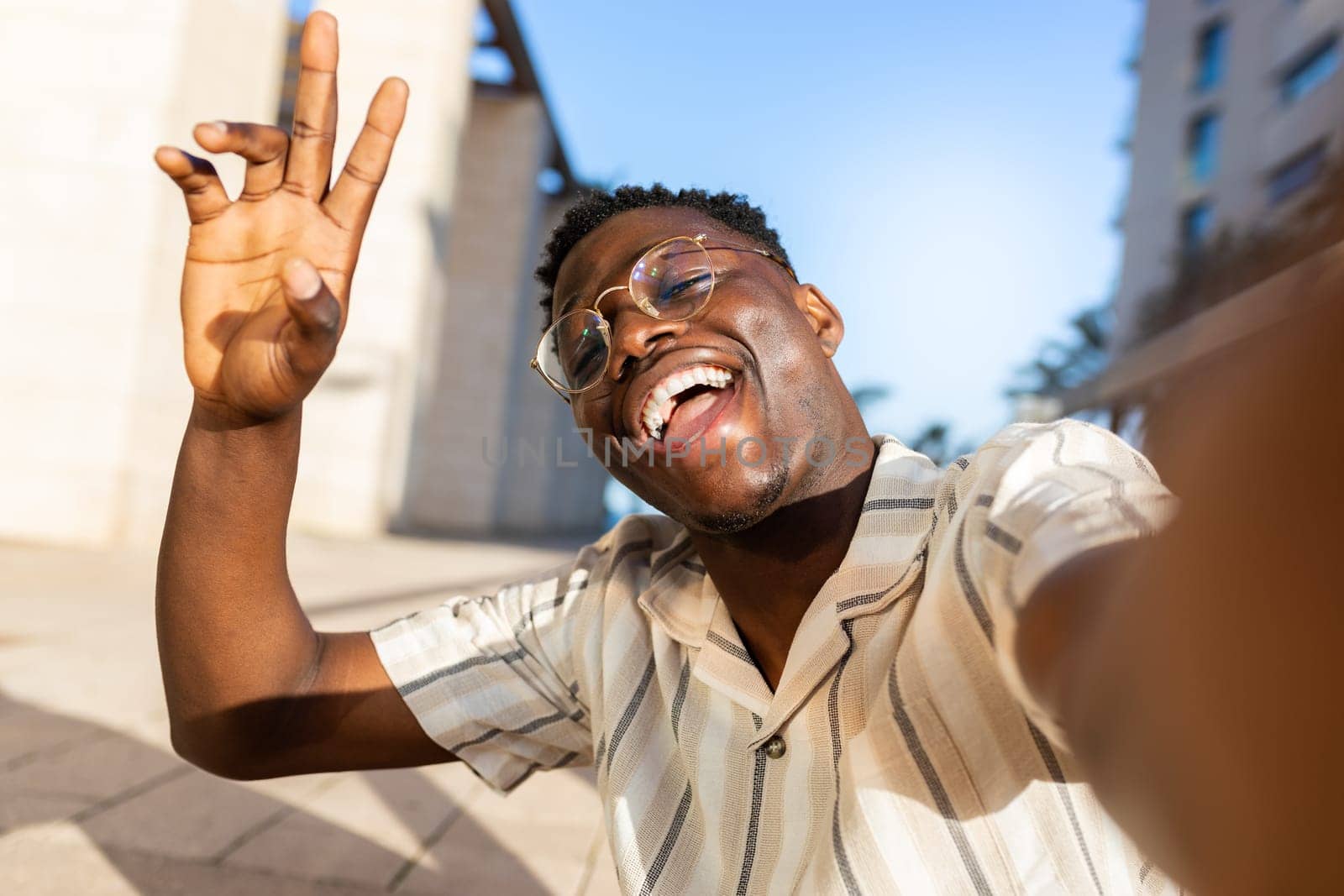 African american man with glasses taking selfie outdoors looking at camera waving hand. Lifestyle concept.