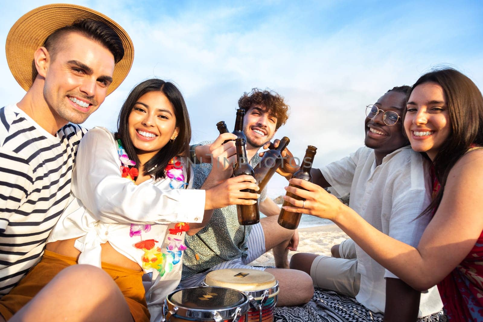 Happy multiracial group of friends toasting with beer together at beach picnic party looking at camera. Vacation and friendship concept.