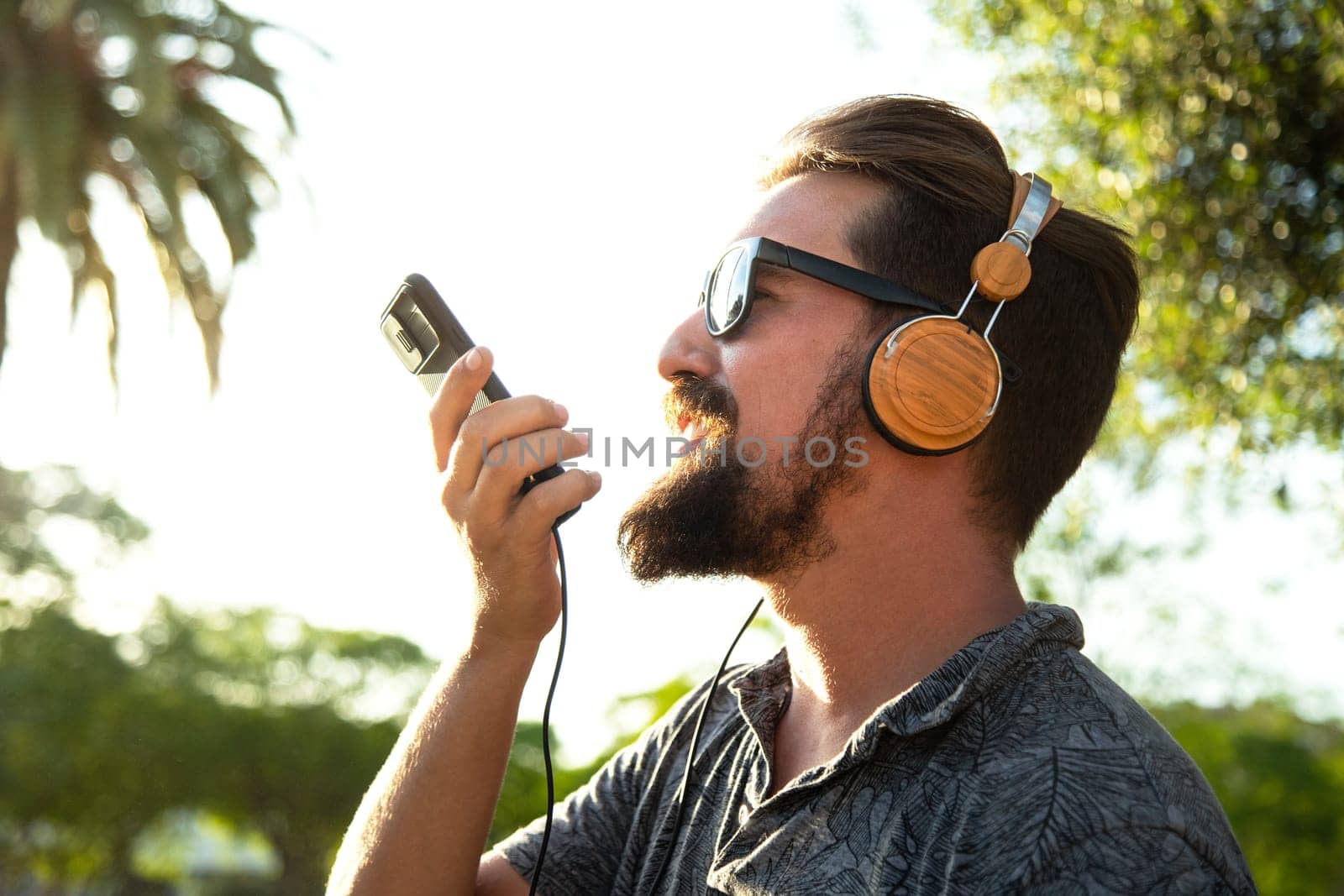 Side view of caucasian male recording voice message using mobile phone outdoors. Lifestyle concept.