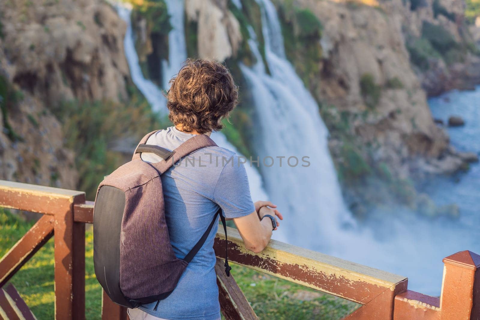 Man tourist on the background of Duden waterfall in Antalya. Famous places of Turkey. Lower Duden Falls drop off a rocky cliff falling from about 40 m into the Mediterranean Sea in amazing water clouds. Tourism and travel destination photo in Antalya, Turkey. Turkiye.