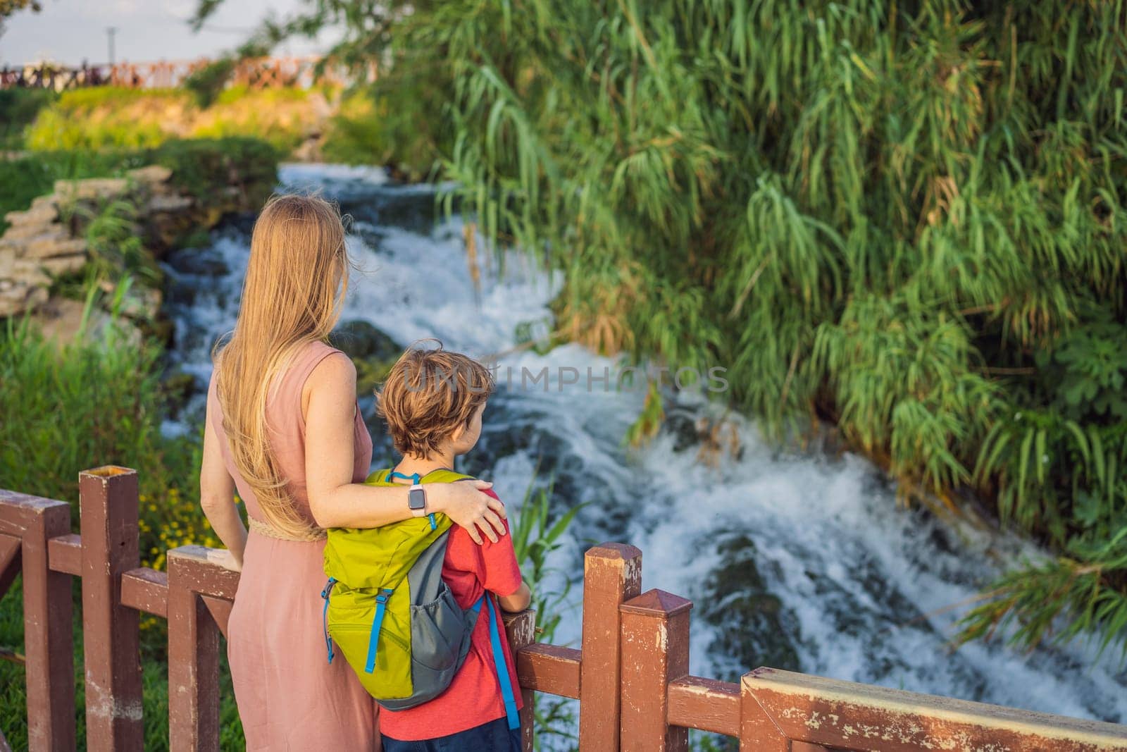 Mother and son tourists on the background of Duden waterfall in Antalya. Famous places of Turkey. Lower Duden Falls drop off a rocky cliff falling from about 40 m into the Mediterranean Sea in amazing water clouds. Tourism and travel destination photo in Antalya, Turkey. Turkiye.