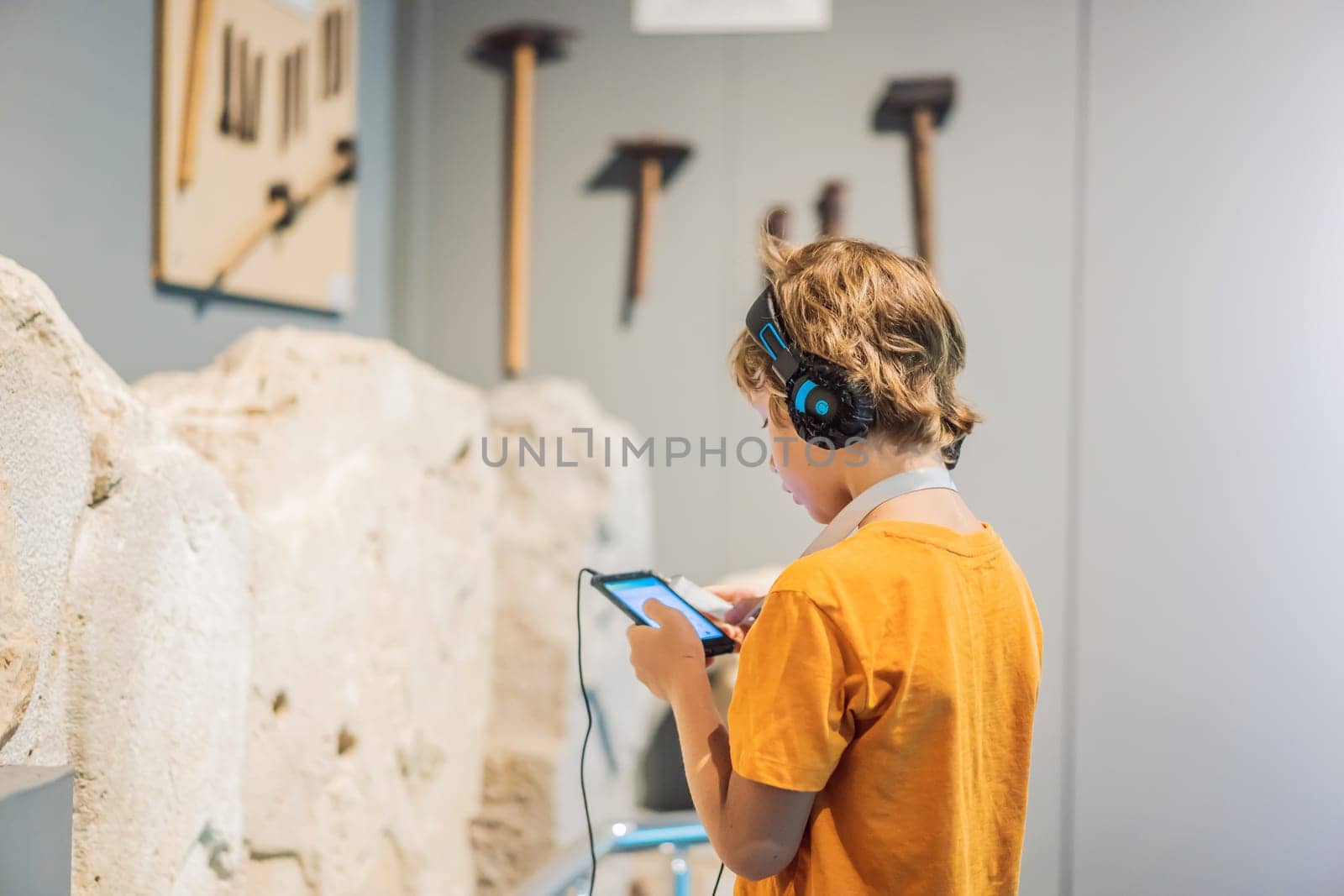 Boy looking at sculptures and listening to audio guide at museum exhibition.