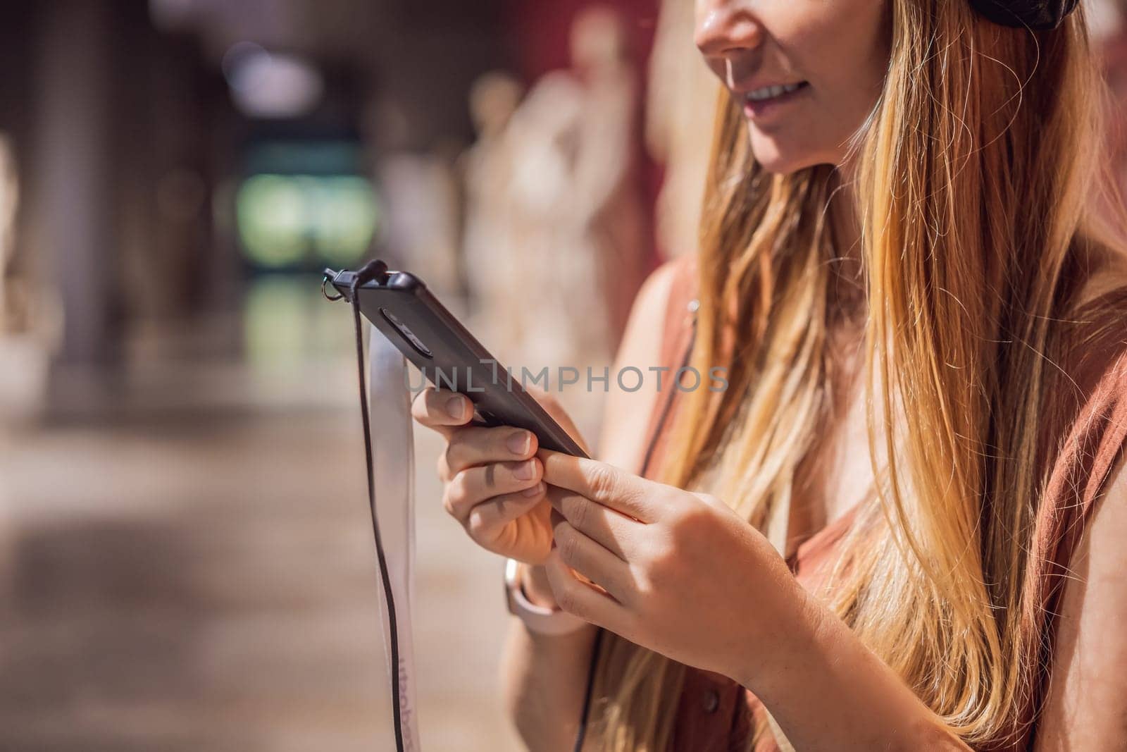 Portrait of contemporary young woman looking at sculptures and listening to audio guide at museum exhibition.