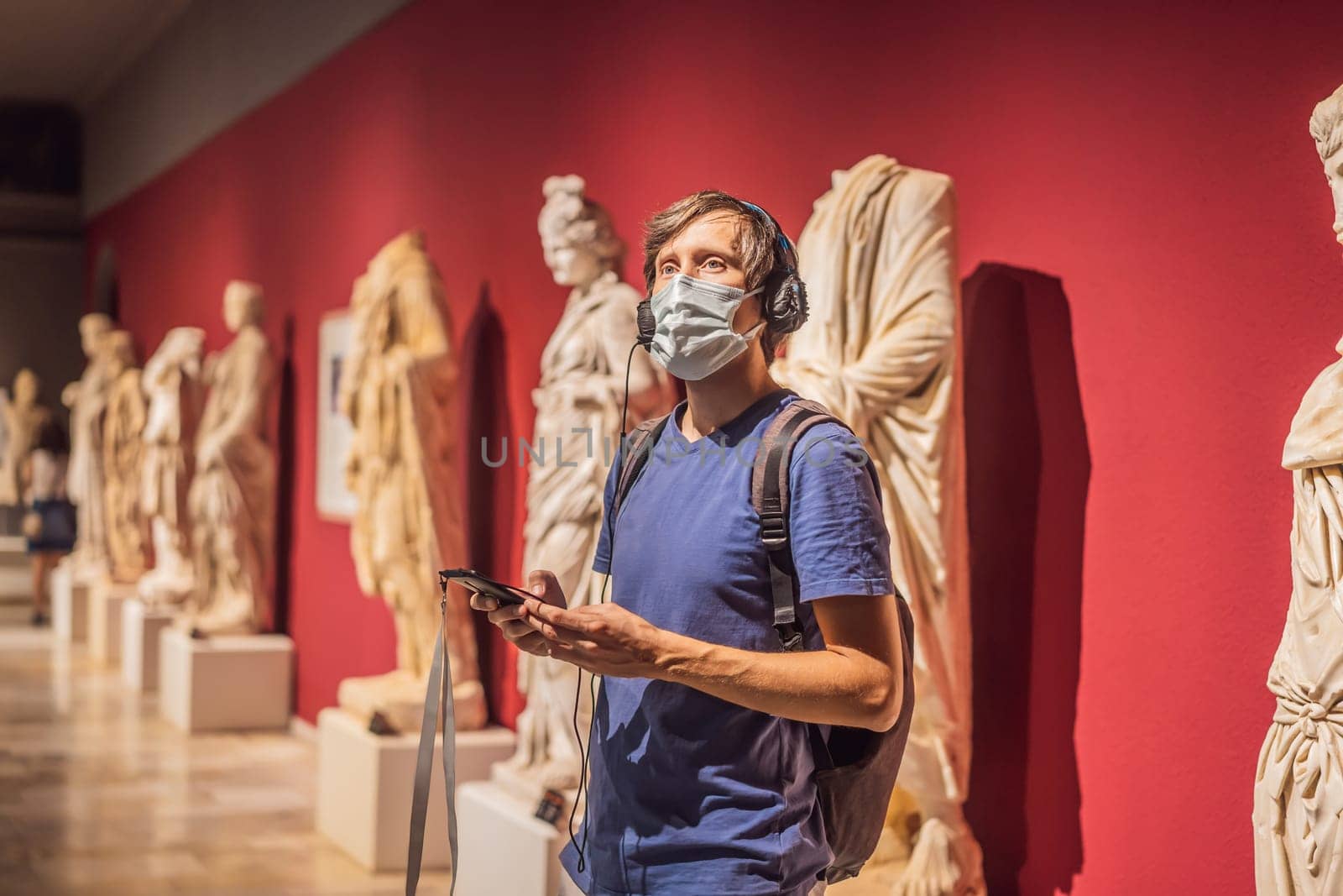 Portrait of contemporary man looking at sculptures and listening to audio guide at museum exhibition.