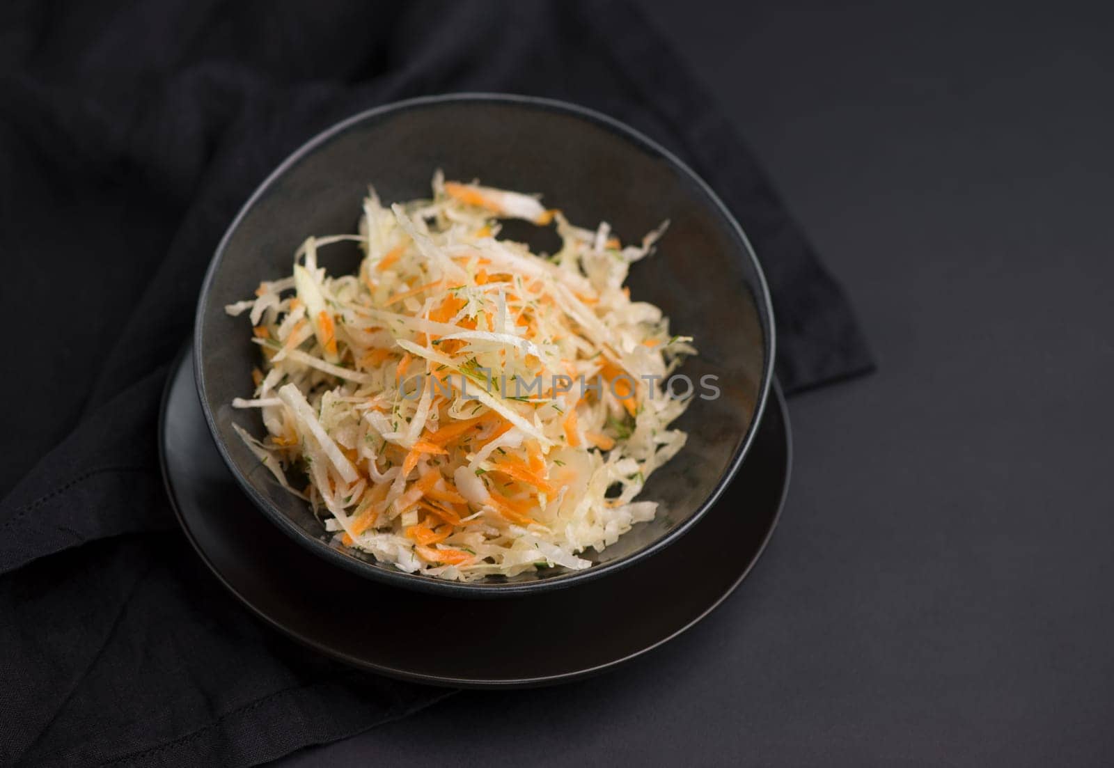 Cabbage salad. Homemade salad of cabbage, carrots and apples in a wooden bowl on a dark background top view.