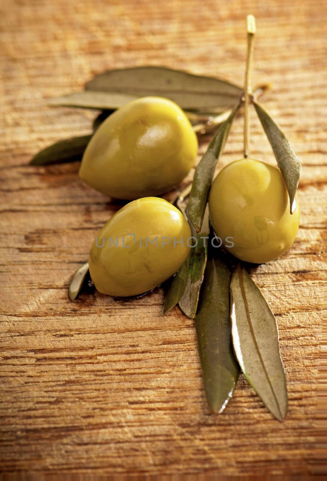 Green olives with leaves on wooden background, top view, flat lay