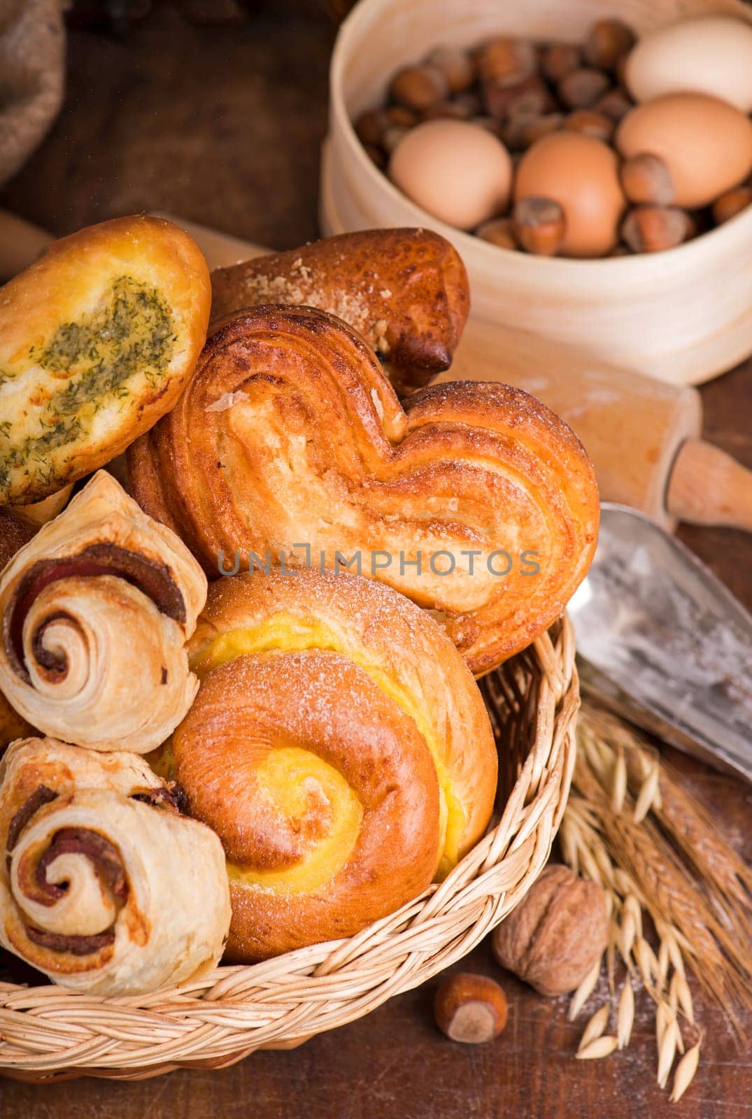 Flour products of various types. Wicker basket with different types of bread and sweet buns on a wooden table. by aprilphoto