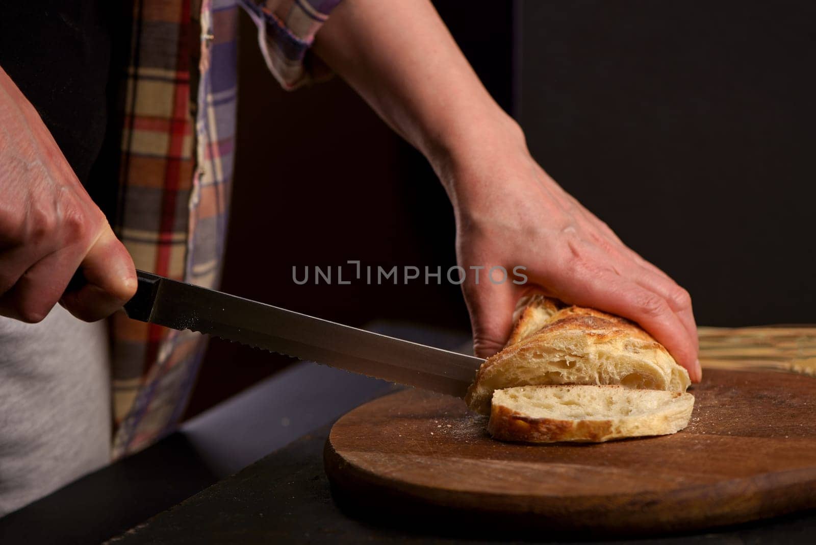 Fresh bread on table close-up. Fresh bread on the kitchen table The healthy eating and traditional bakery concept. Front viev. Whole grain bread put on kitchen wood plate with a chef holding knife for cut.