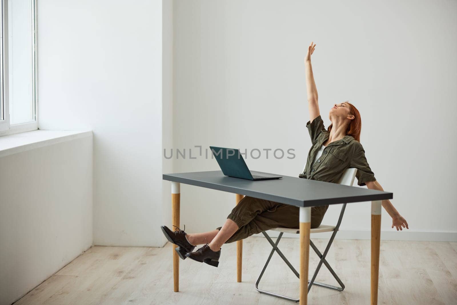 a very happy woman sits at a laptop and rejoices at the completed tasks raising her hands up. High quality photo