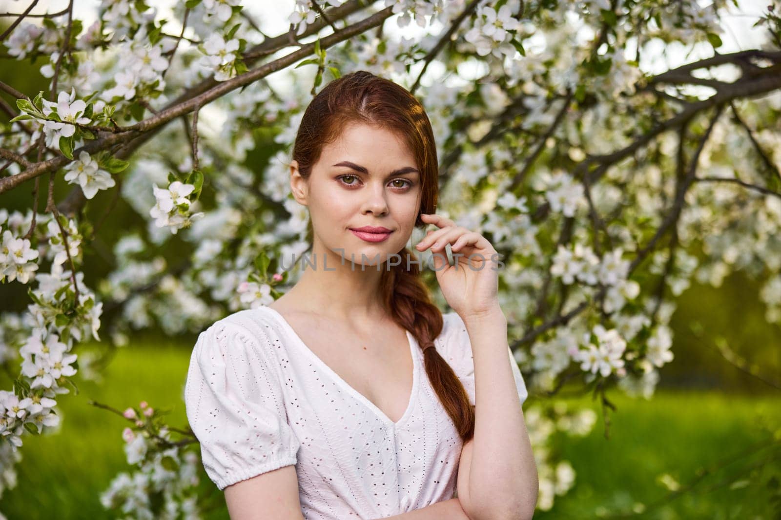 portrait of a young beautiful woman in a white dress among the branches of a flowering apple tree. High quality photo