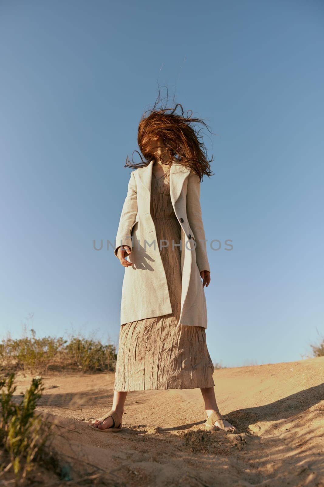 stylish woman in a light jacket posing in nature covering her face with hair by Vichizh
