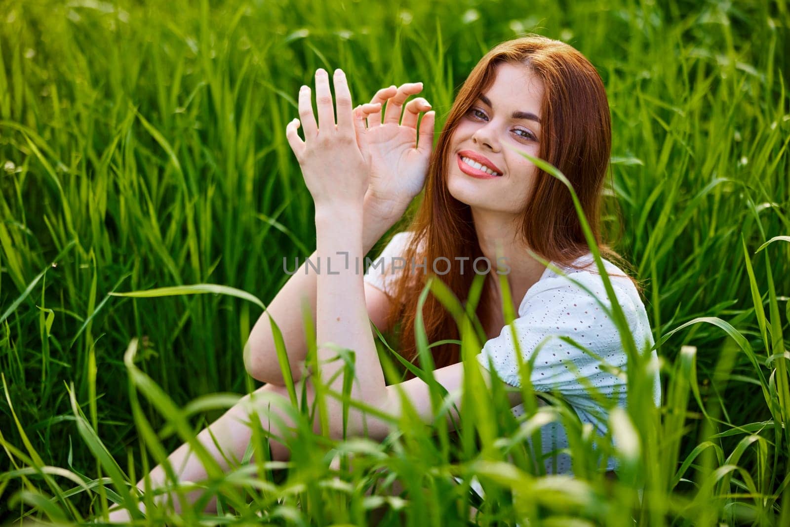 portrait of a beautiful, happy woman sitting in the grass in a light dress and smiling at the camera. High quality photo