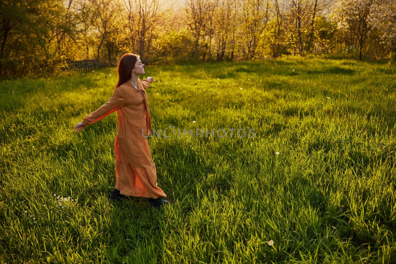 a joyful woman runs through a green field with her hands behind her back, enjoying a warm summer day and nature during the sunset. Horizontal photography in nature. High quality photo