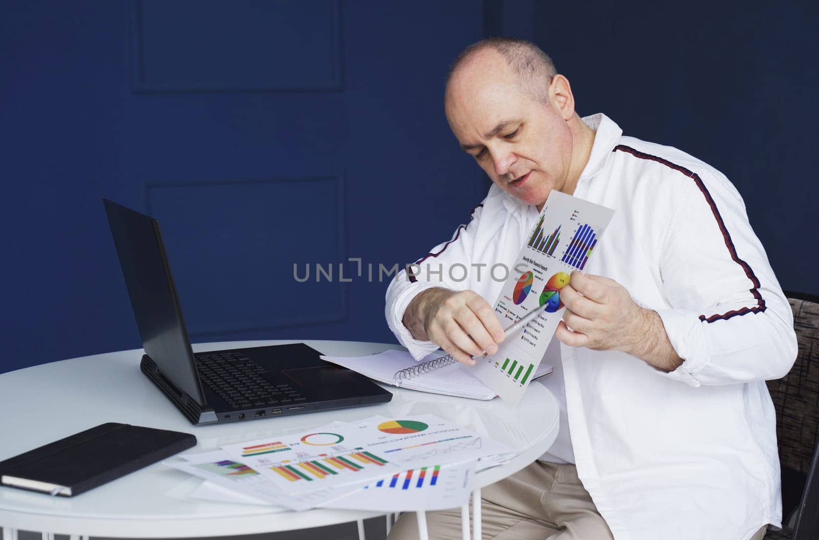 A man makes an online video call chat, sitting at home and talking into a laptop webcam, showing a document.