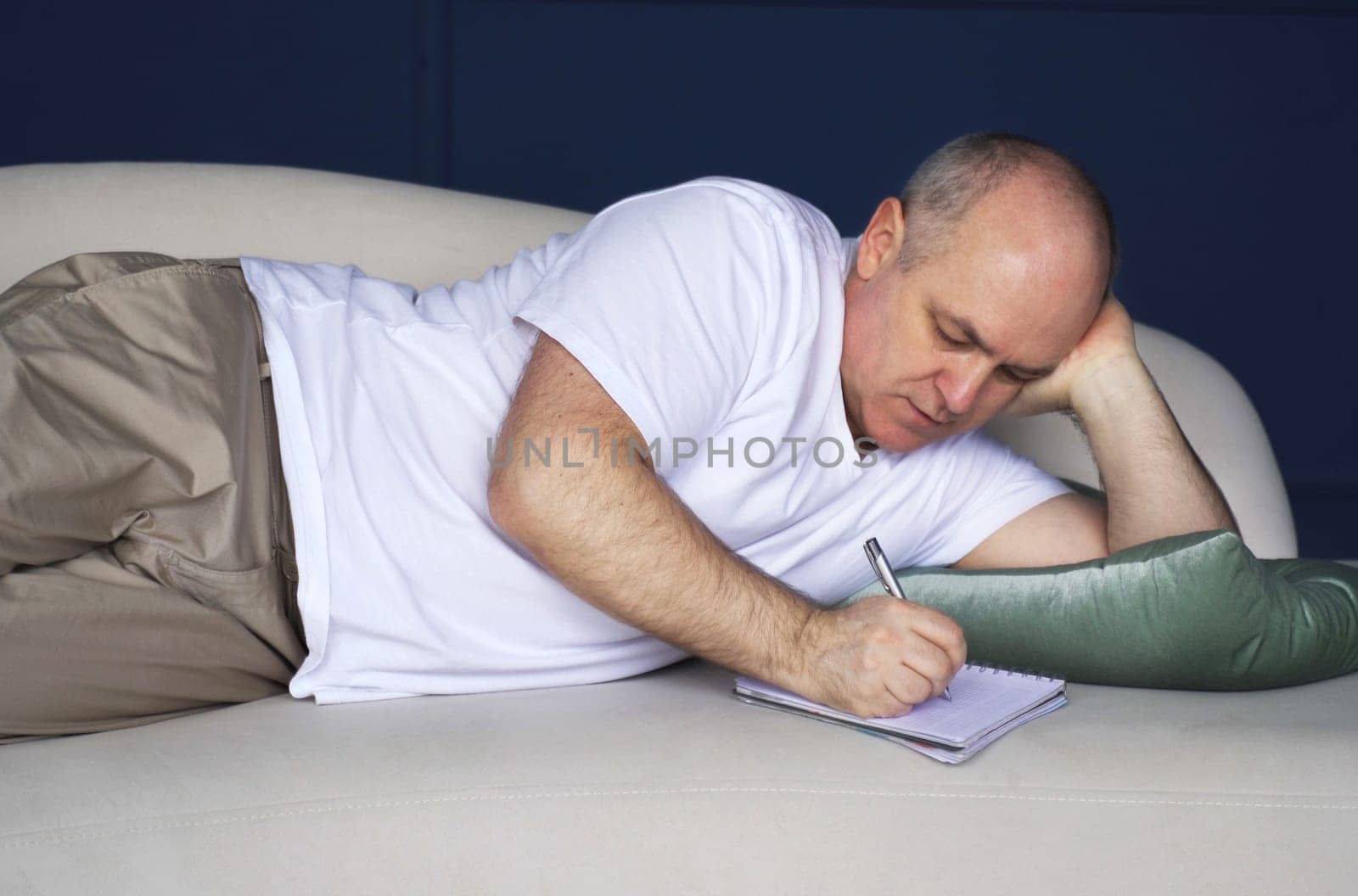 A middle-aged man lies on the couch and makes notes in a notebook. by Sd28DimoN_1976