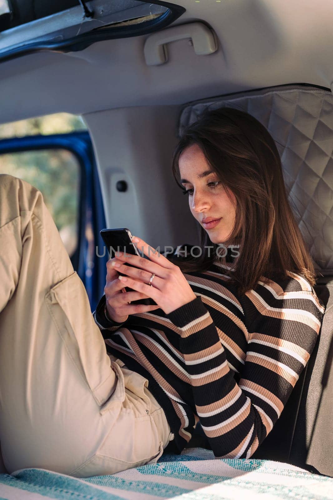 young caucasian woman relaxing in camper van using a mobile phone, concept of road trip adventure and van life relaxation