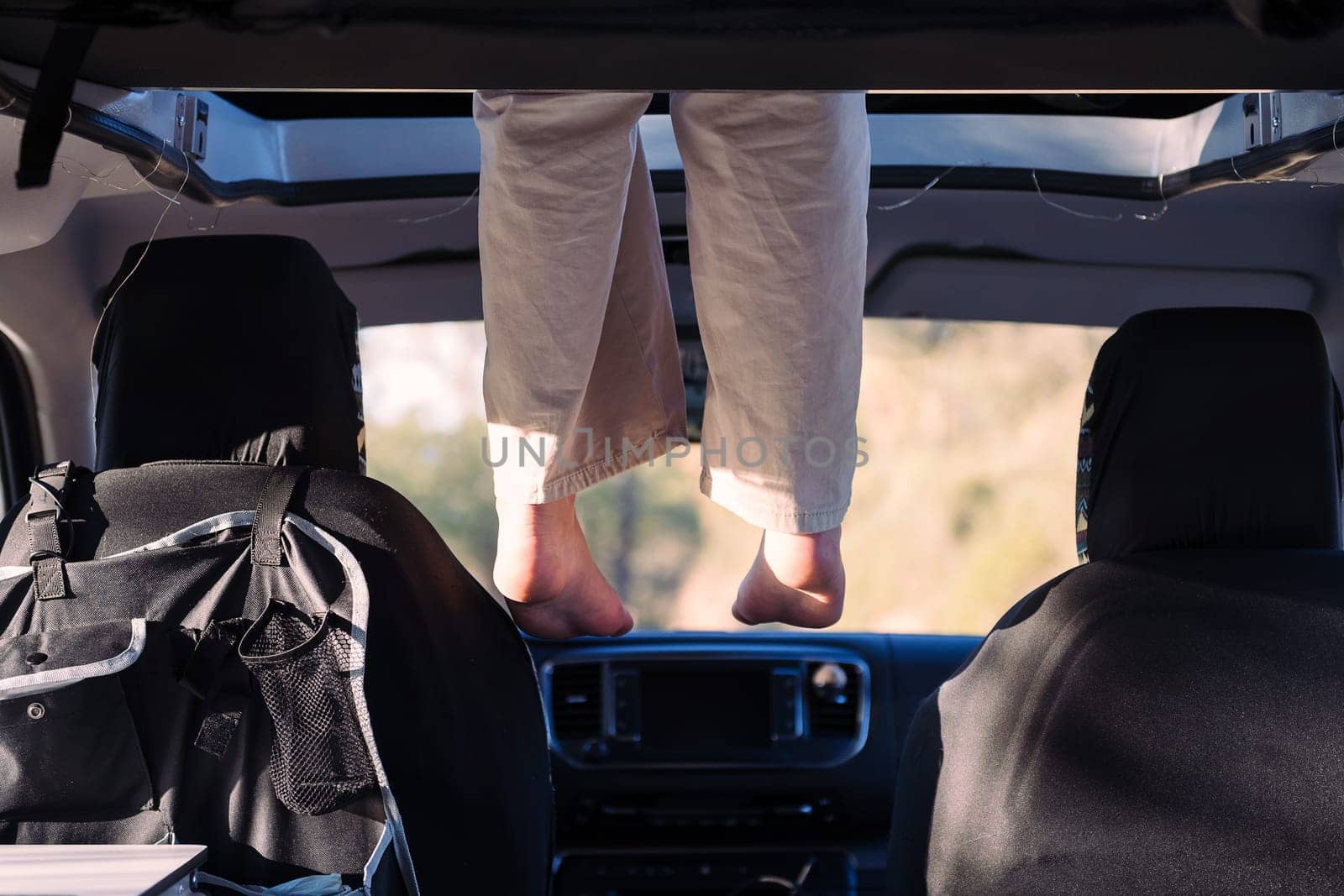 unrecognizable woman relaxing with feet dangling off the elevated bed of a camper van, concept of road trip adventure and van life relaxation