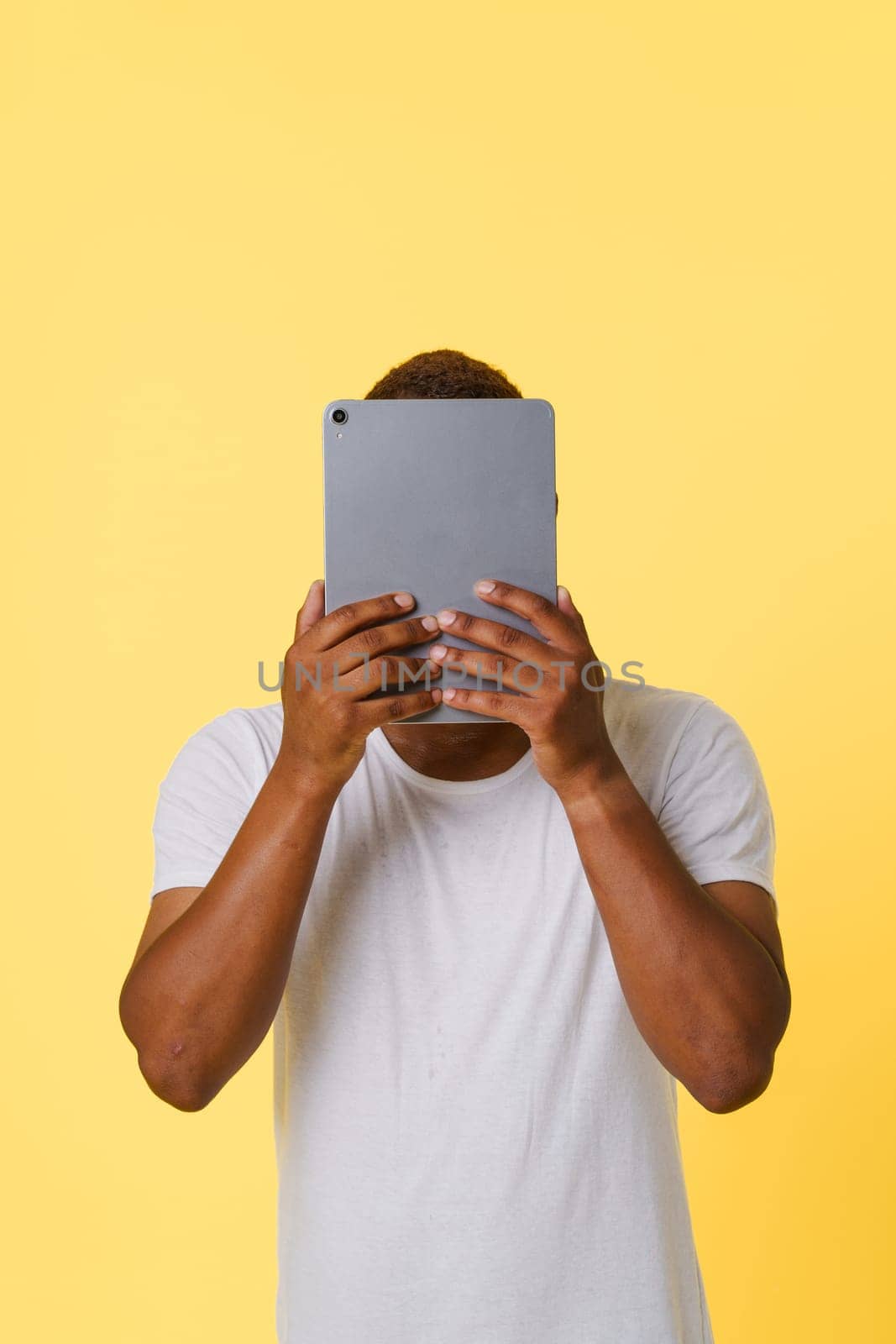 Anonymity incognito online concept. Anonymous African American person holding tablet PC in hands, with hidden face isolated on bright yellow background with copy space for designers to add their own text or graphics. High quality photo