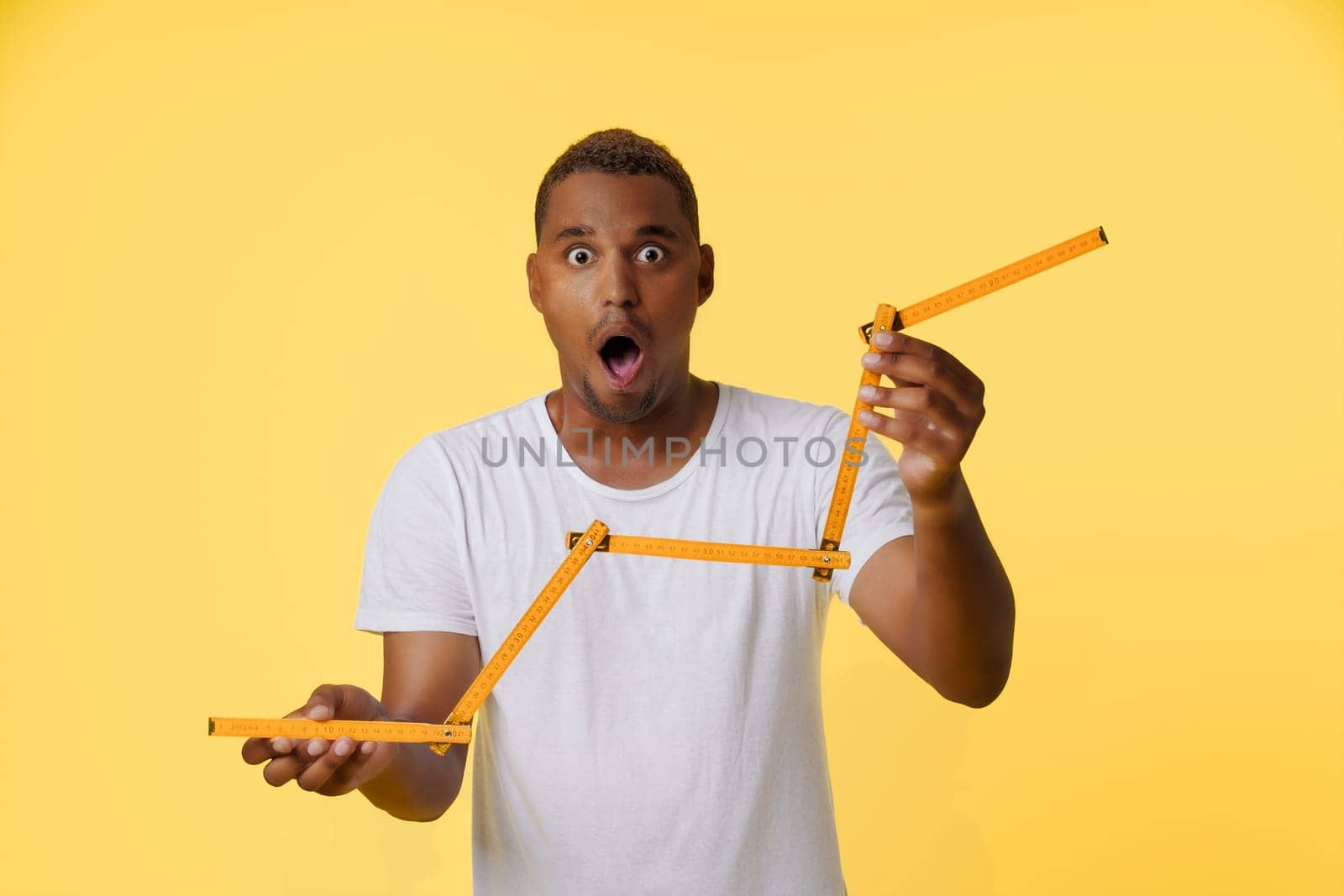 Concept of income growth, amazed African American man holding folding ruler and showing growth chart on the stock exchange. Man is standing on bright yellow background with copy space for designers to add their own text or graphics. High quality photo