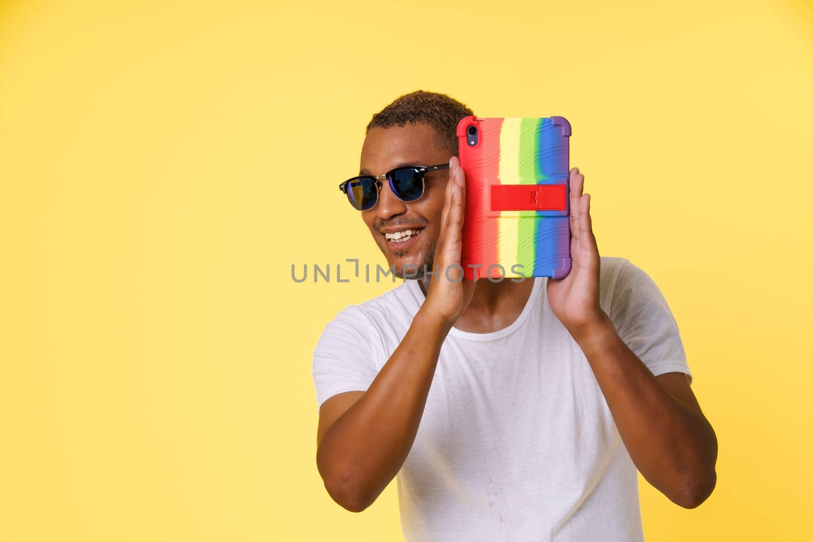 With smile on face, young African American man uses Tablet PC to share truth and come out as gay. Yellow background and ample copy space for LGBT community or concepts of bravery and self-expression. by LipikStockMedia