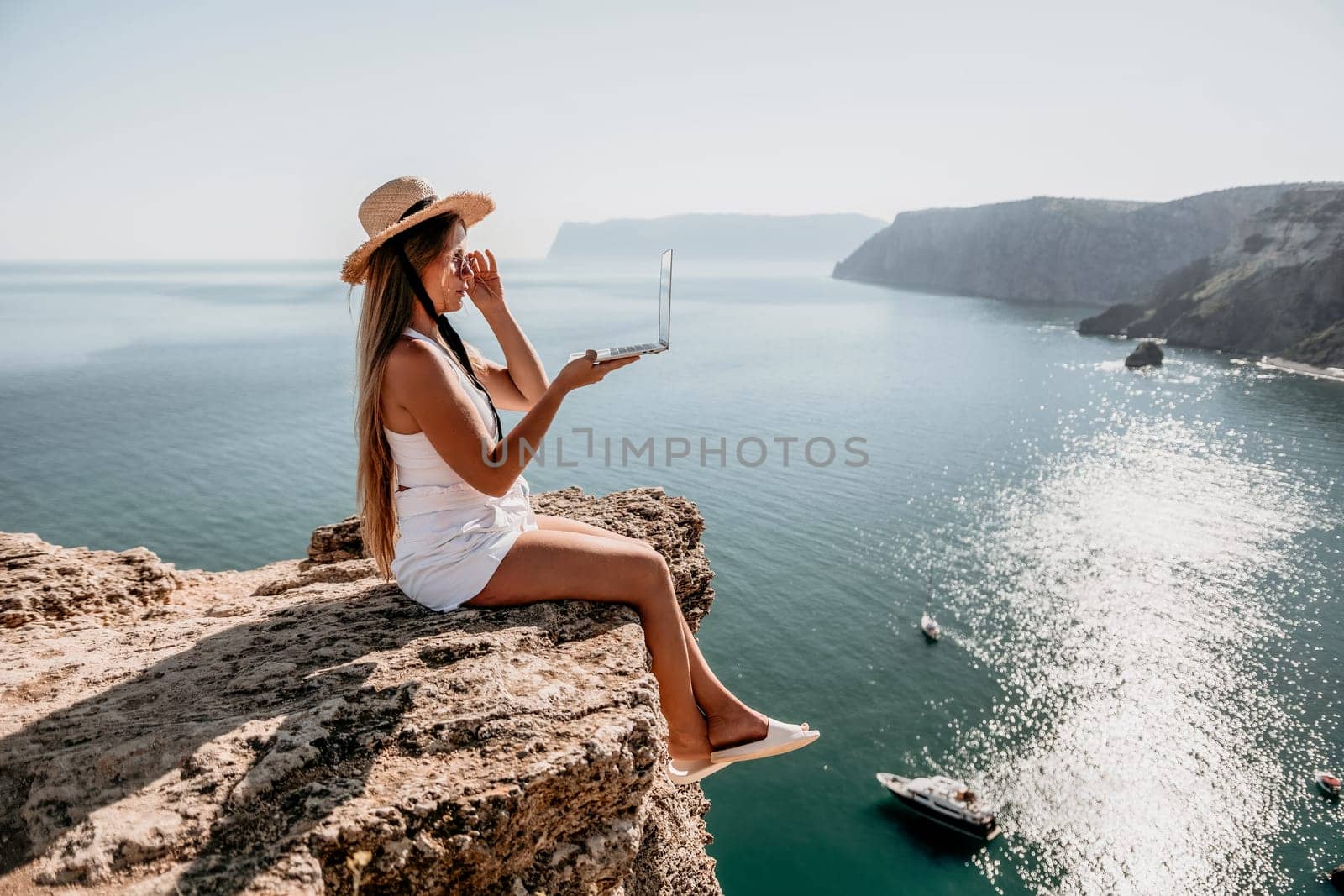 Woman laptop sea. Working remotely on seashore. Happy successful woman female freelancer in straw hat working on laptop by the sea at sunset. Freelance, remote work on vacation by panophotograph