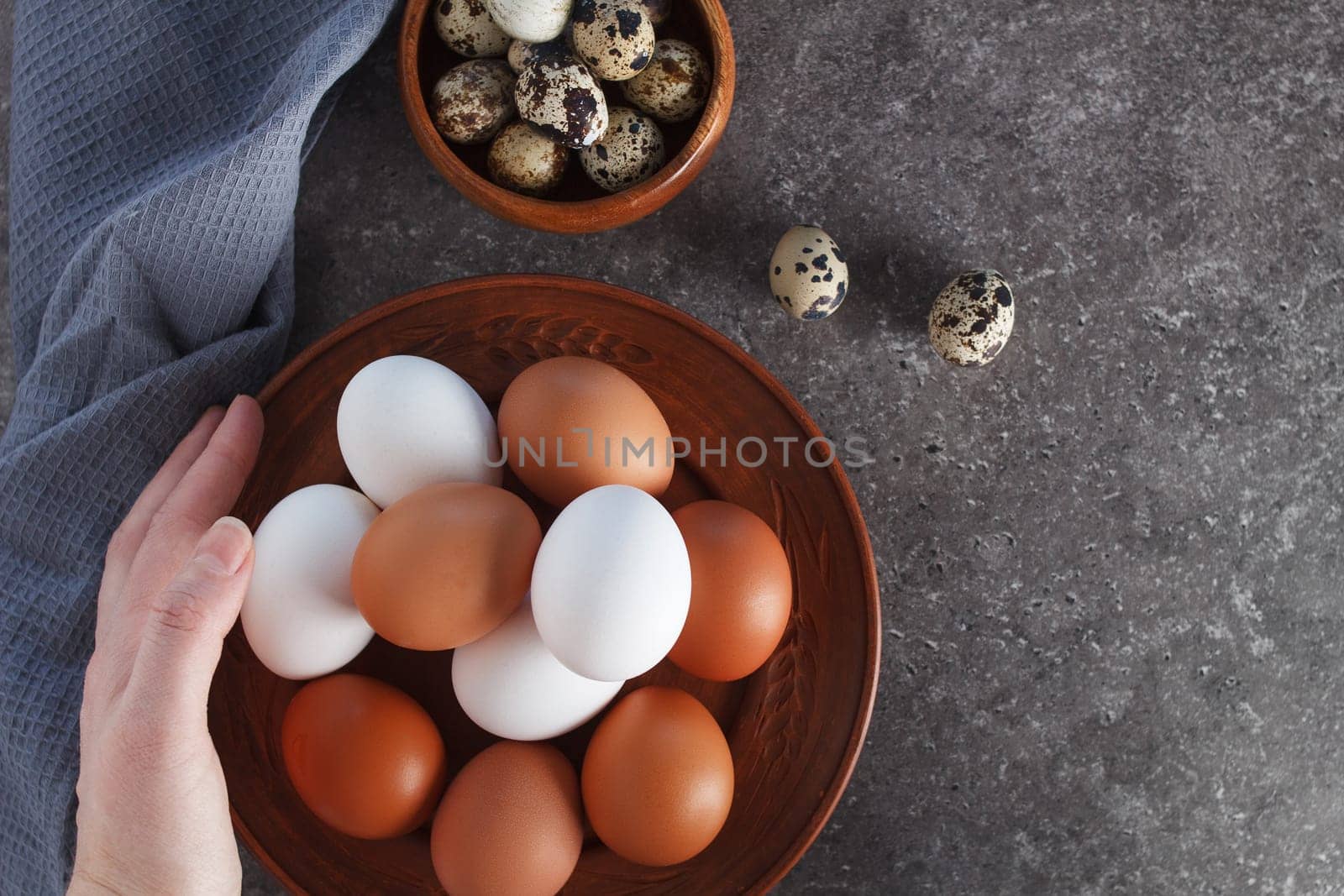 A woman's hand holds a chicken egg over a plate of eggs on the kitchen table. by lara29