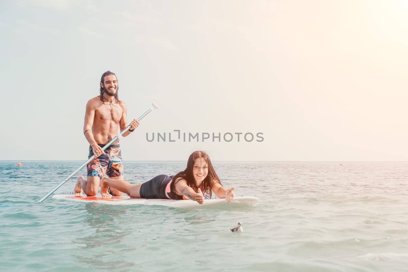 Silhouette of woman standing, surfing on SUP board, confident paddling through water surface. Idyllic sunset or sunrise. Sports active lifestyle at sea or river.