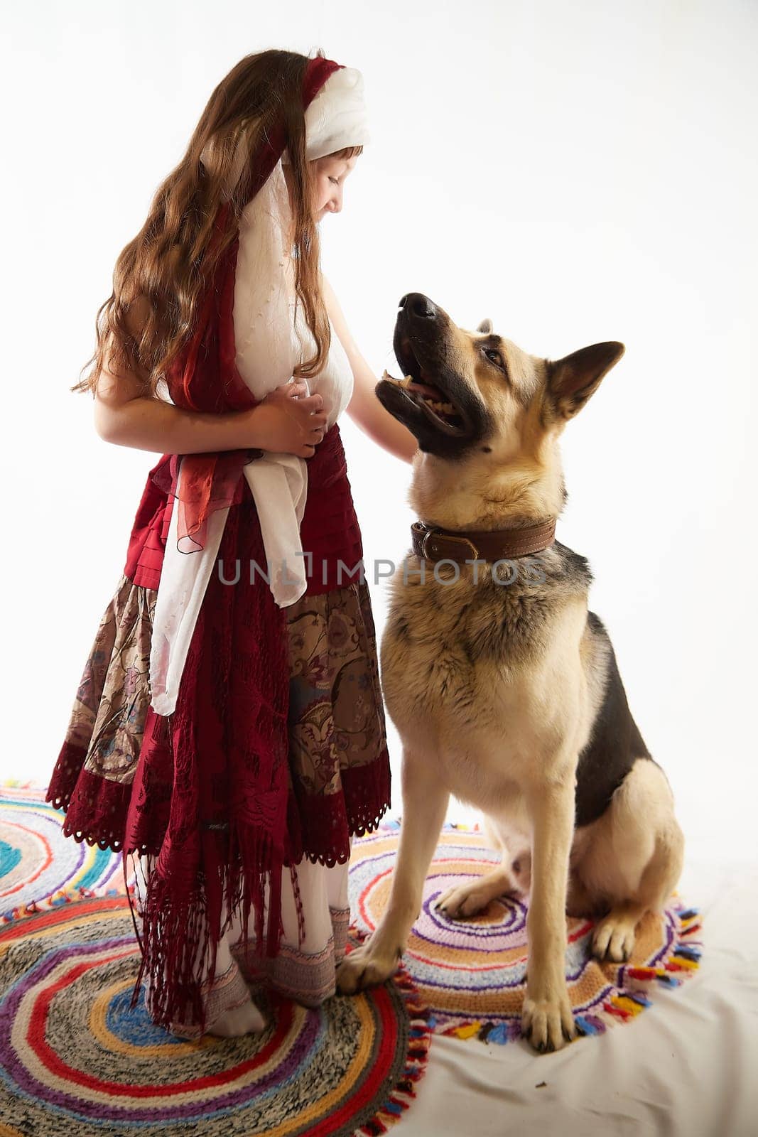 Portrait of Little girl in a stylized Tatar national costume with big shepherd dog on a white background in the studio. Photo shoot of funny young teenager who is not a professional model