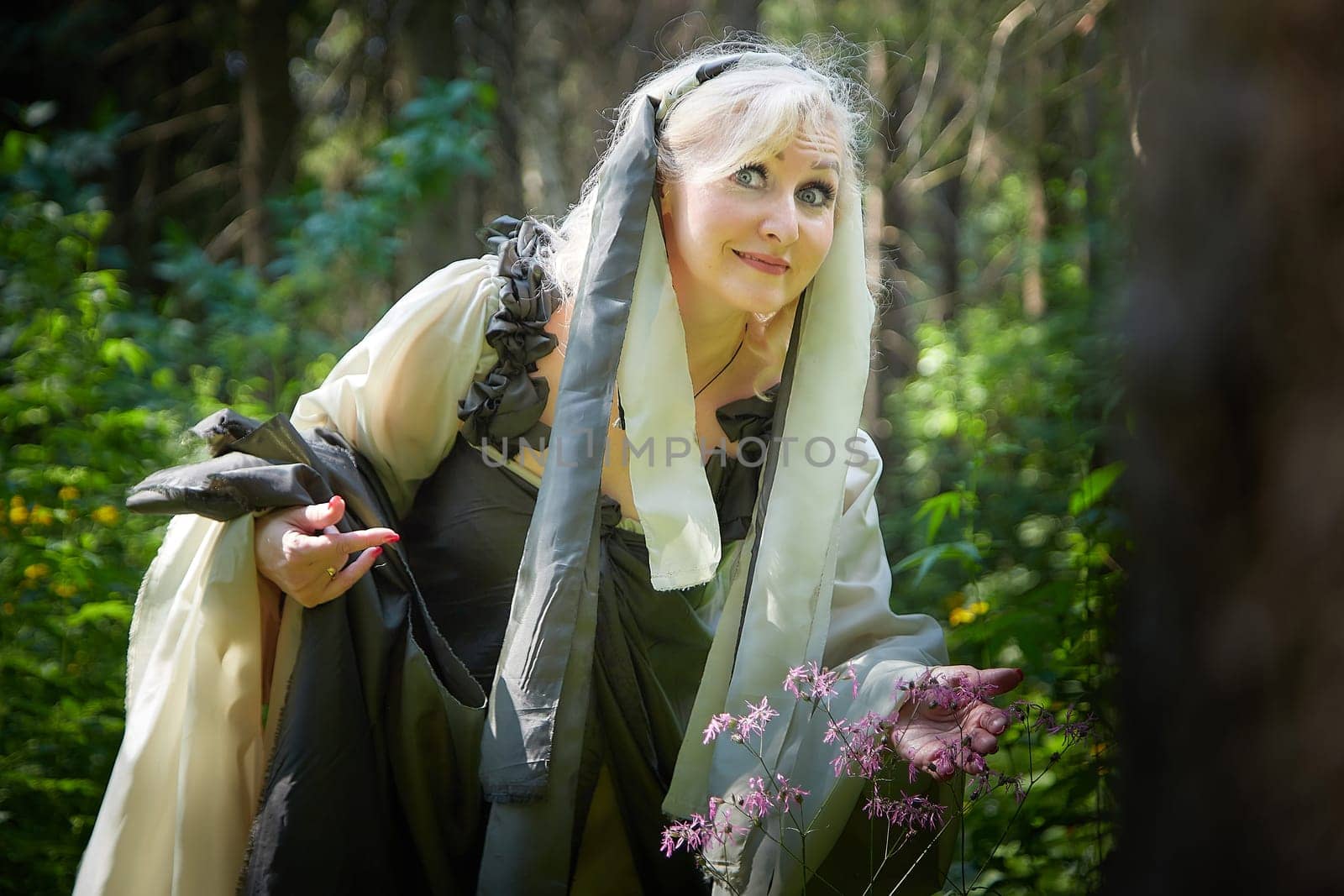 Adult mature woman 40-60 in a green long fairy dress in forest. Photo shoot in style of dryad and queen of nature. Fairy in beautiful green summer forest. Concept of caring for nature