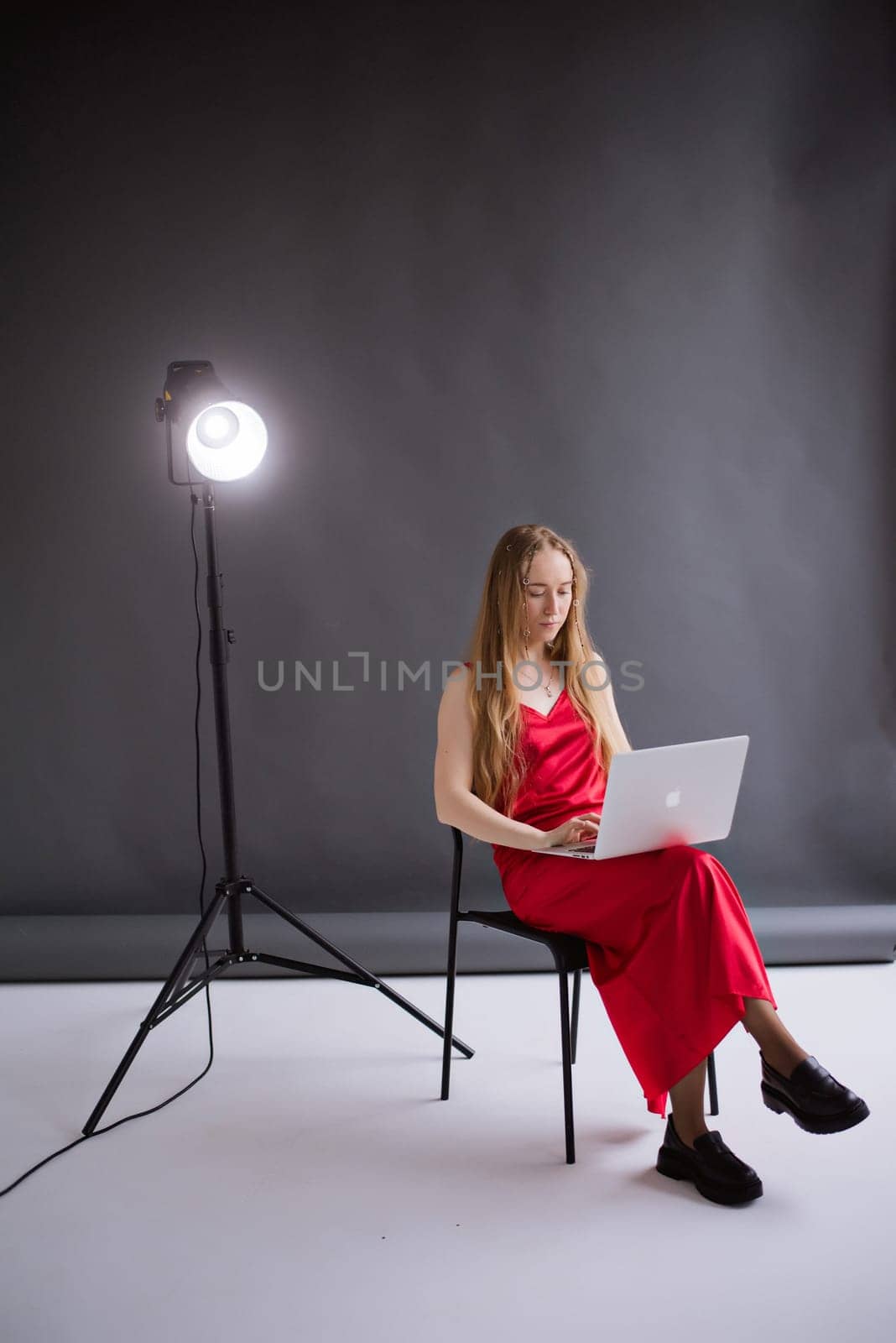 A business woman blogger in a red dress is working, typing on a laptop apple and sitting on a chair. portrait blonde assistant of hands with computer MacBook . Vertical