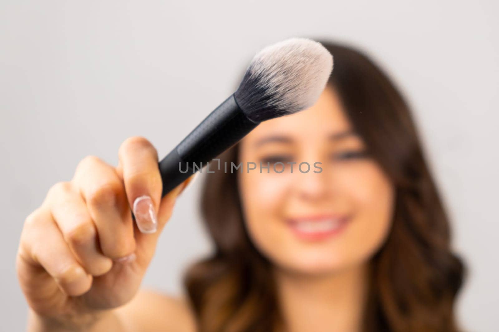 Young brunette model holding of big brush for applzing powder in front of face, selective focus