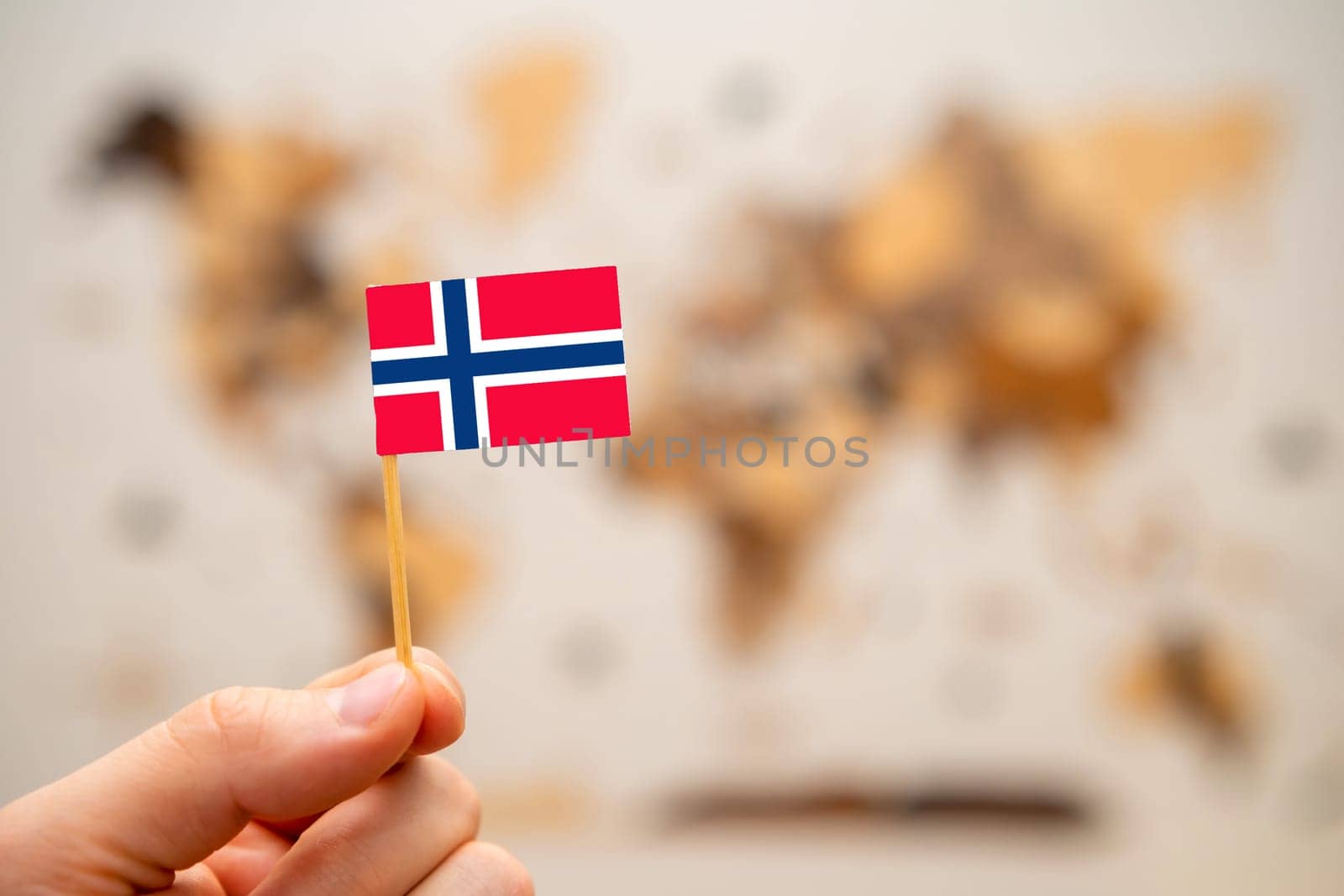Norway flag in mans hand on the wooden world map background. Global economy and geopolitics concept.