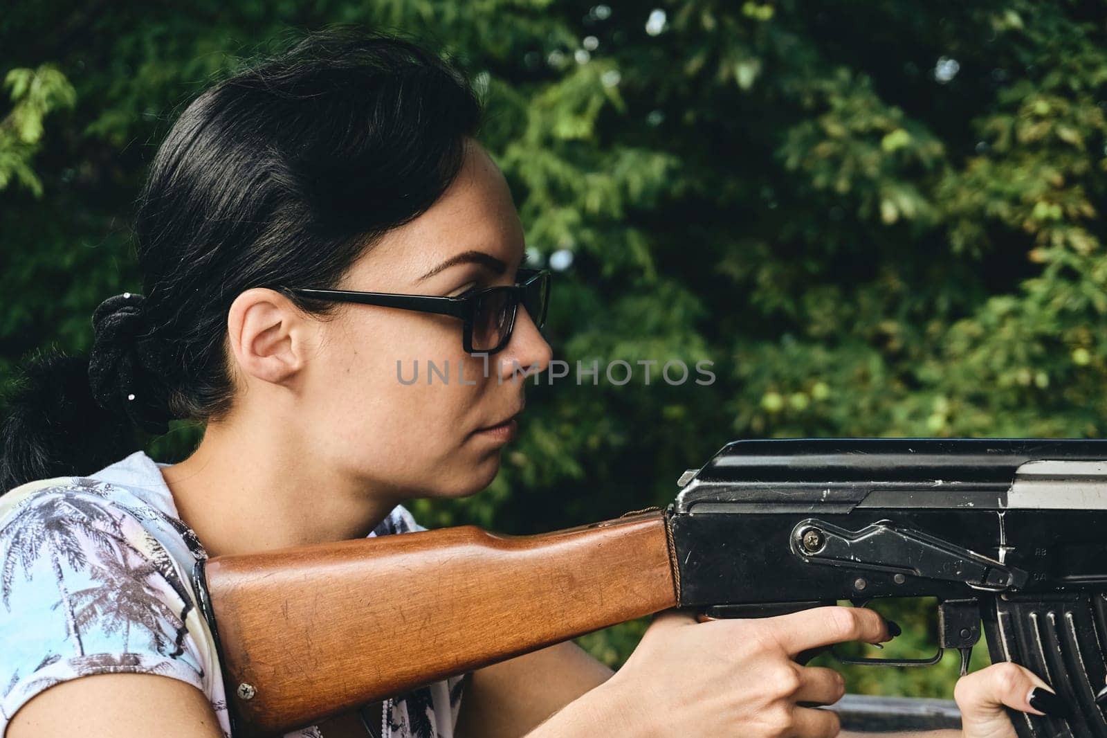 a weapon incorporating a metal tube from which bullets, shells, or other missiles are propelled by explosive force. A young girl in dark sunglasses shoots from a machine gun and green trees.