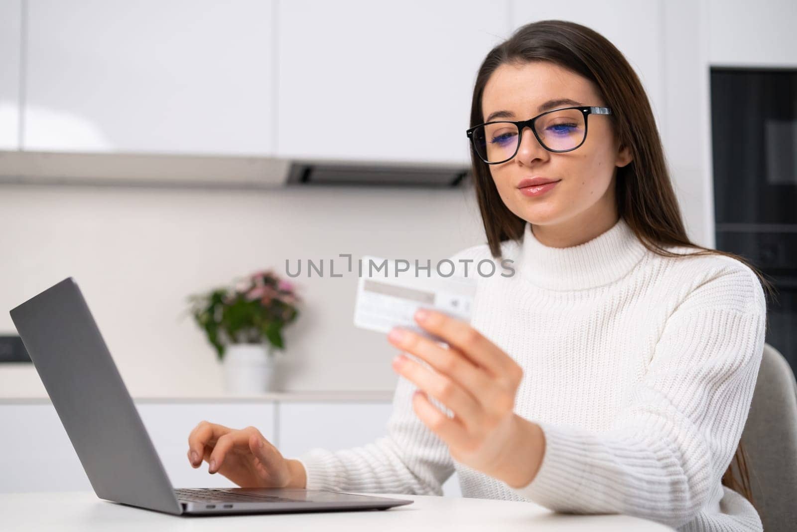 Woman enters card details into laptop to buy educational courses. Brunette lady sits in the kitchen making online payment closeup