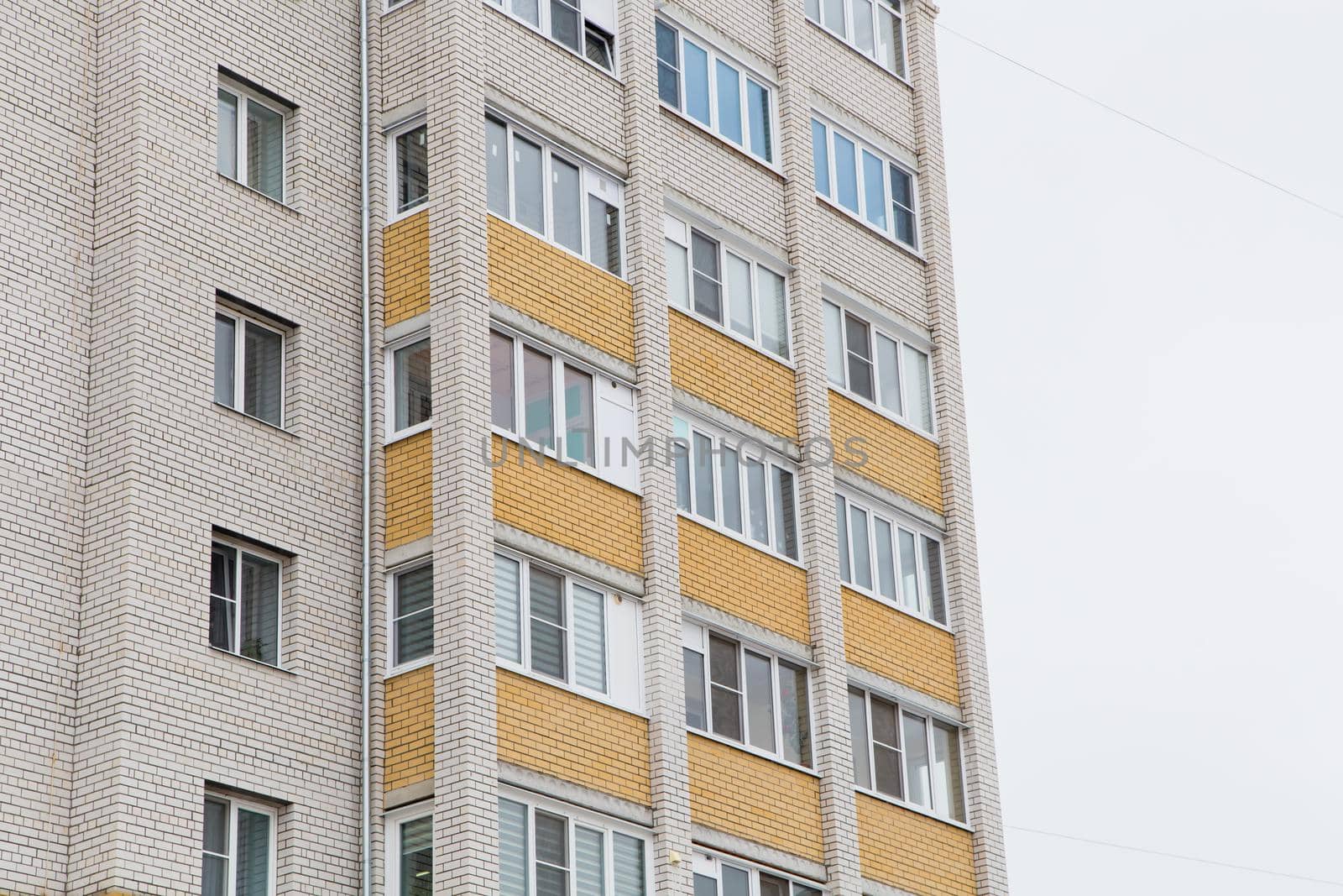 Facade of a high-rise building with plastic windows and balconies. Against the background of the gray sky. Modern new buildings, building facades. Real estate and urban architecture concept.