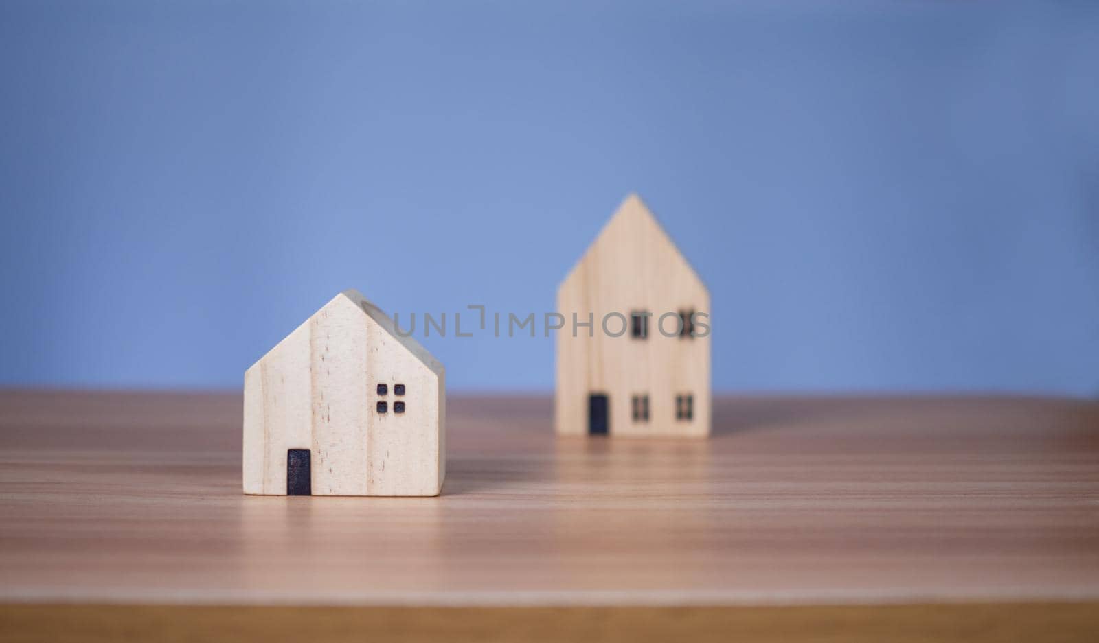 Two wooden model houses placed on a wooden table. with a light blue background